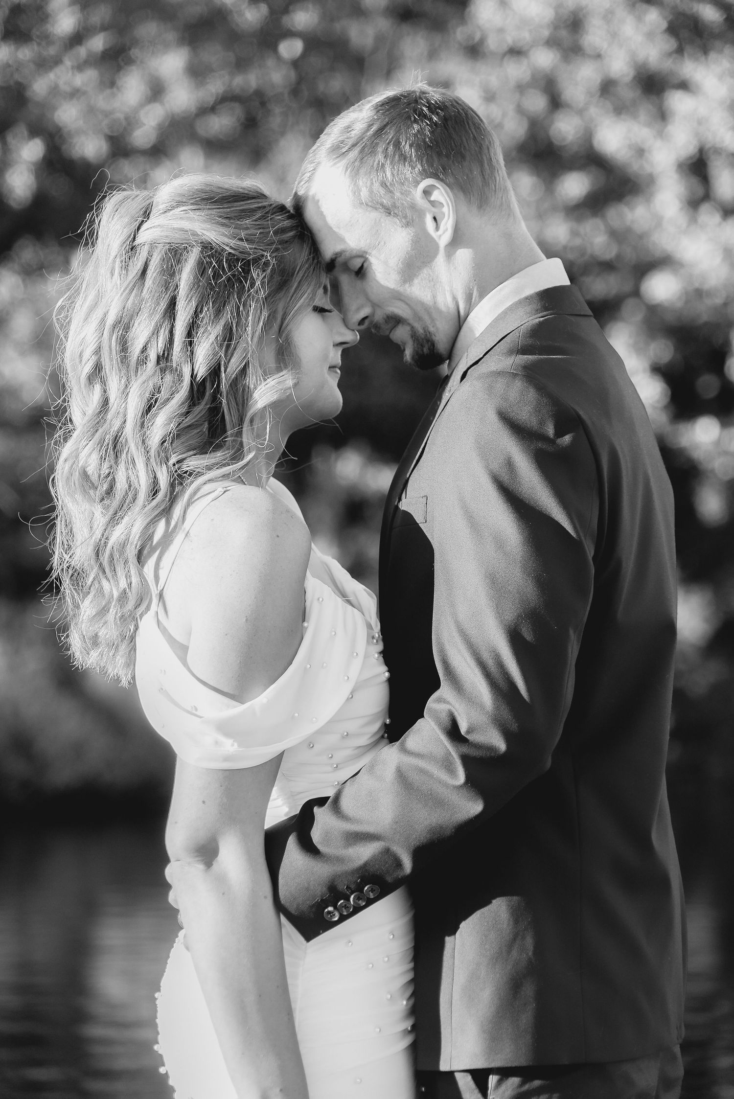 Black and white photo of bride and groom touching foreheads romantically outdoors.