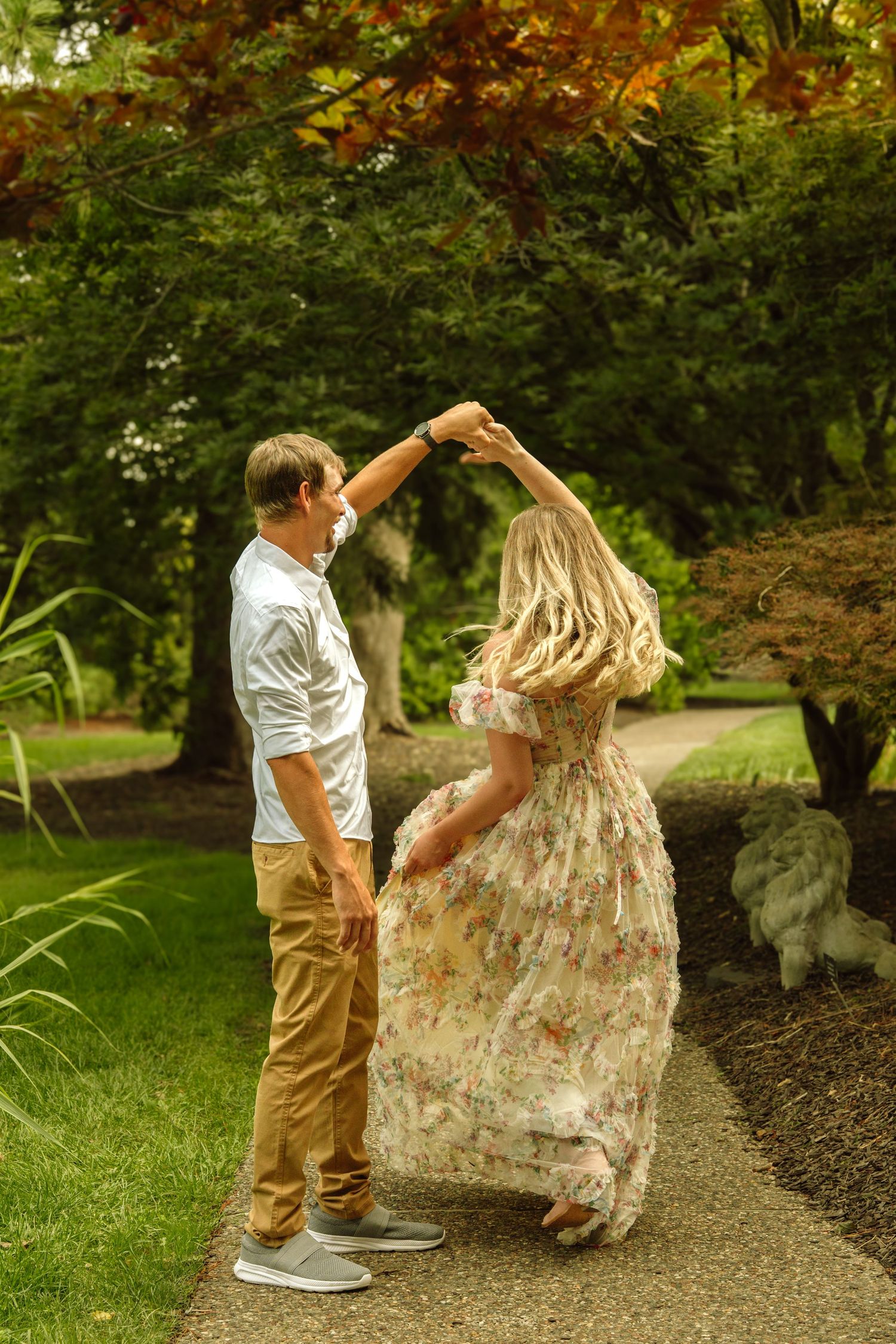 Couple dancing together on a garden path surrounded by colorful autumn trees.