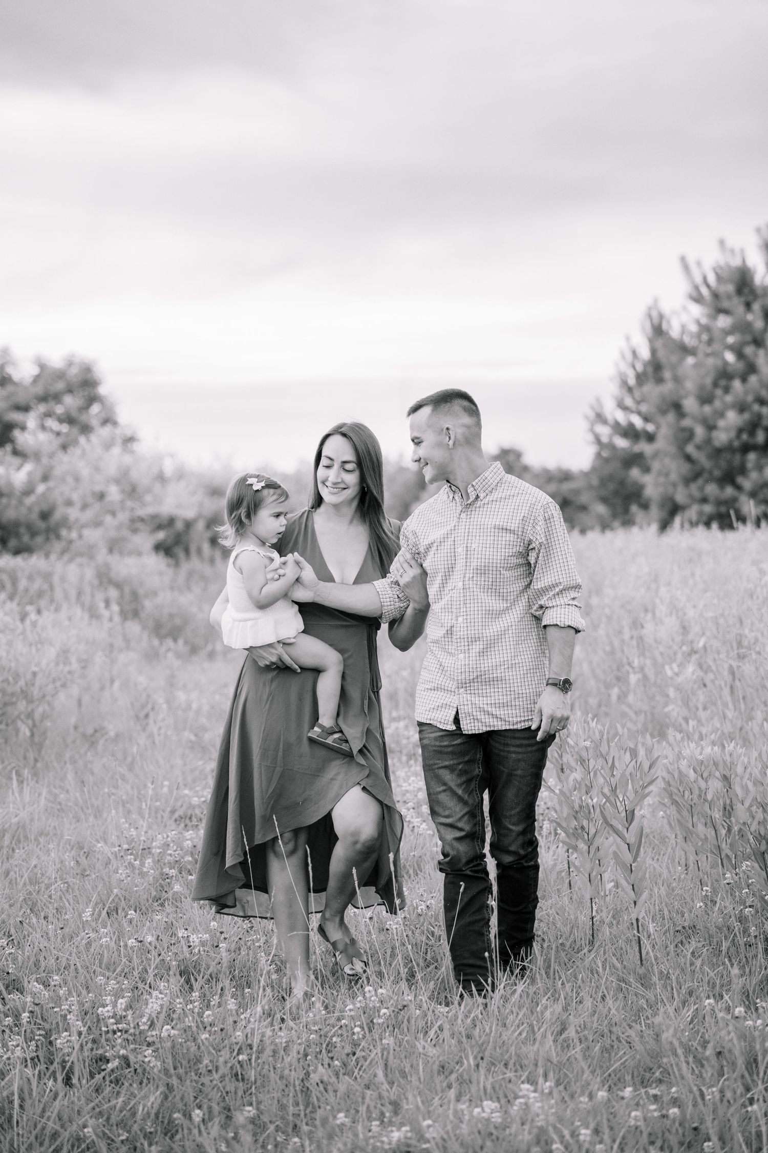 Black and white family portrait of parents with toddler in open meadow field.