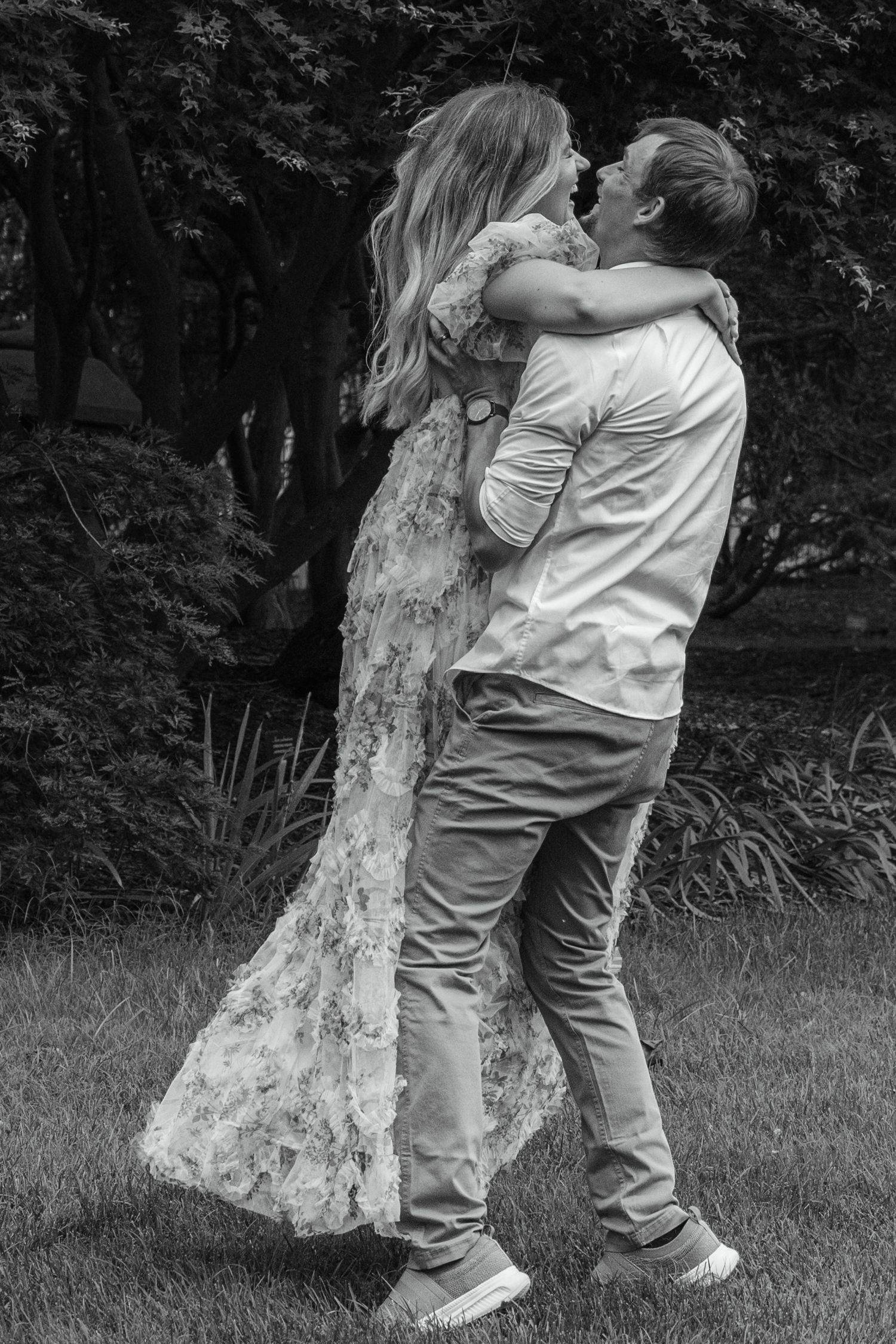 Black and white photo of a couple embracing and kissing outdoors in a garden setting.