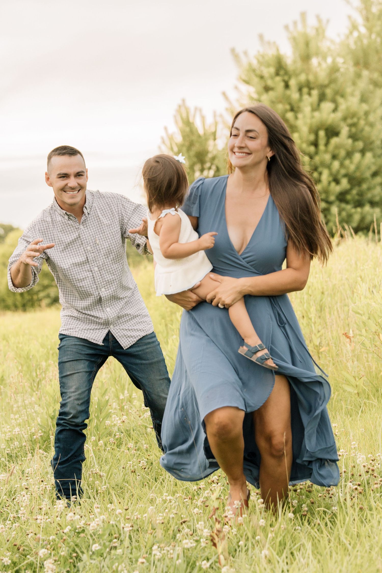 Happy family running and playing together in sunny wildflower meadow on summer day.
