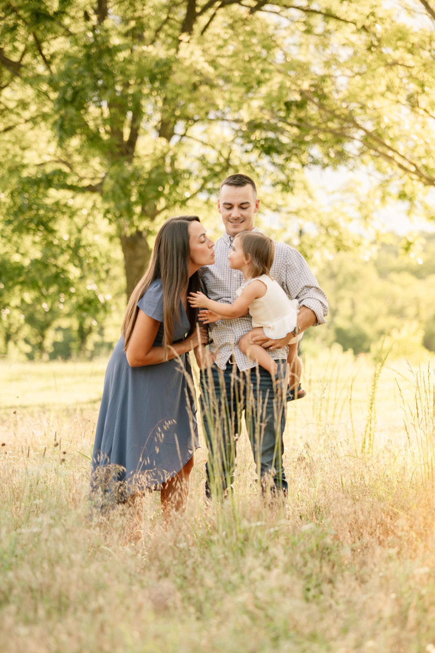A happy young family with a baby enjoys a sunny outdoor photo session in a lush green field.
