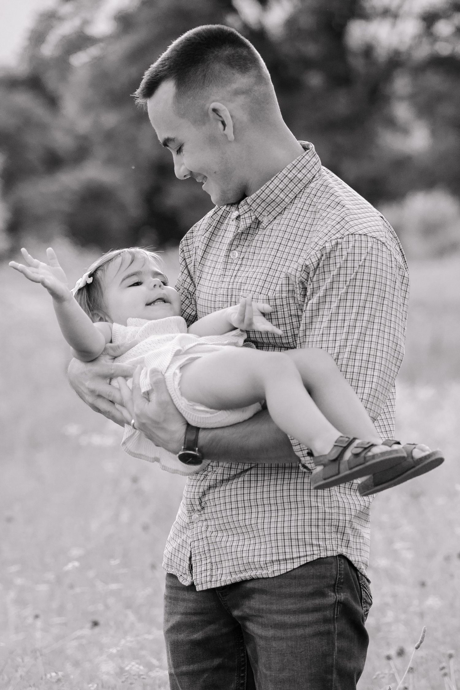 Black and white photo of a smiling father holding his laughing baby girl outdoors in a field.