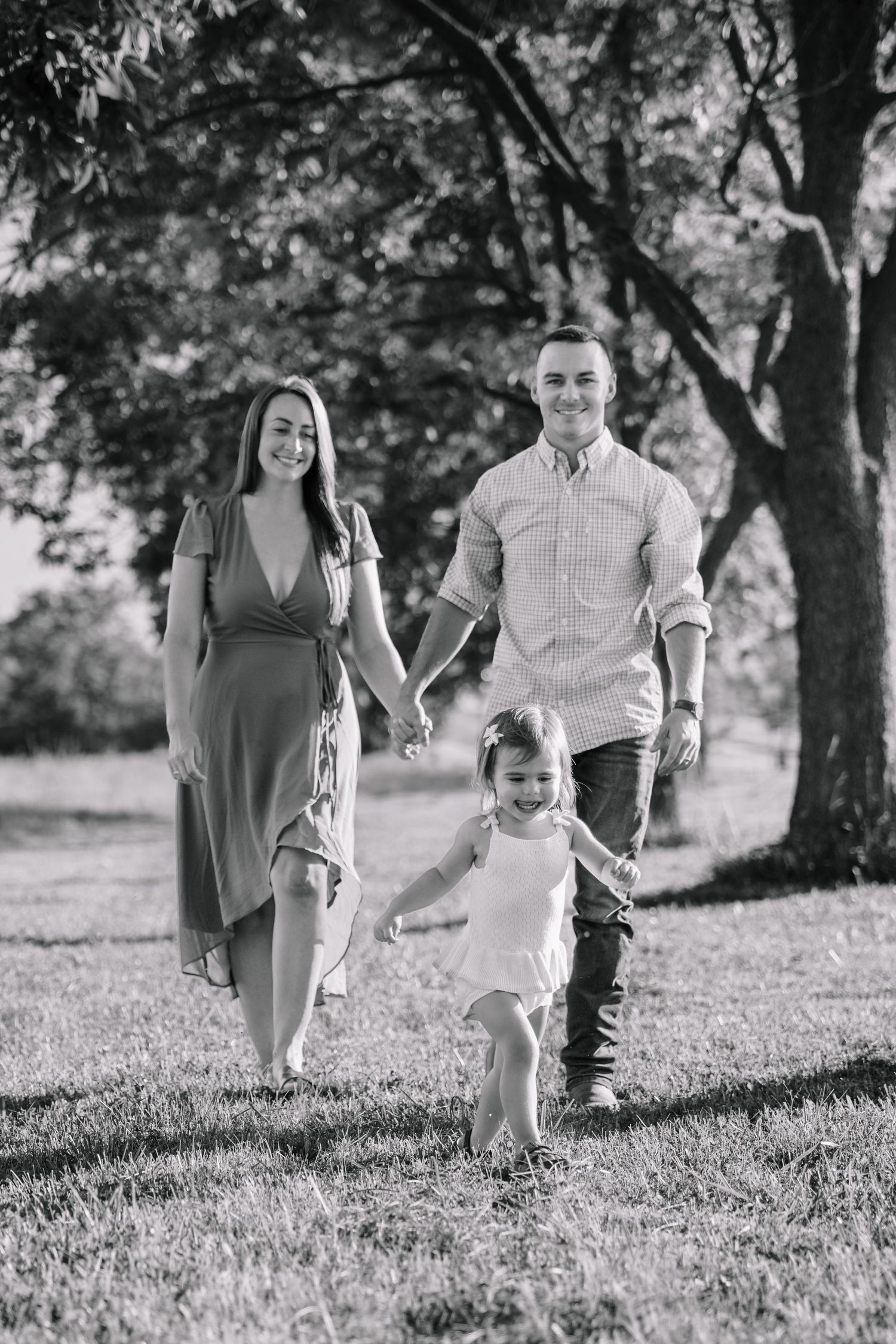 Black and white photo of a happy young family holding hands and walking together in a sunny park.