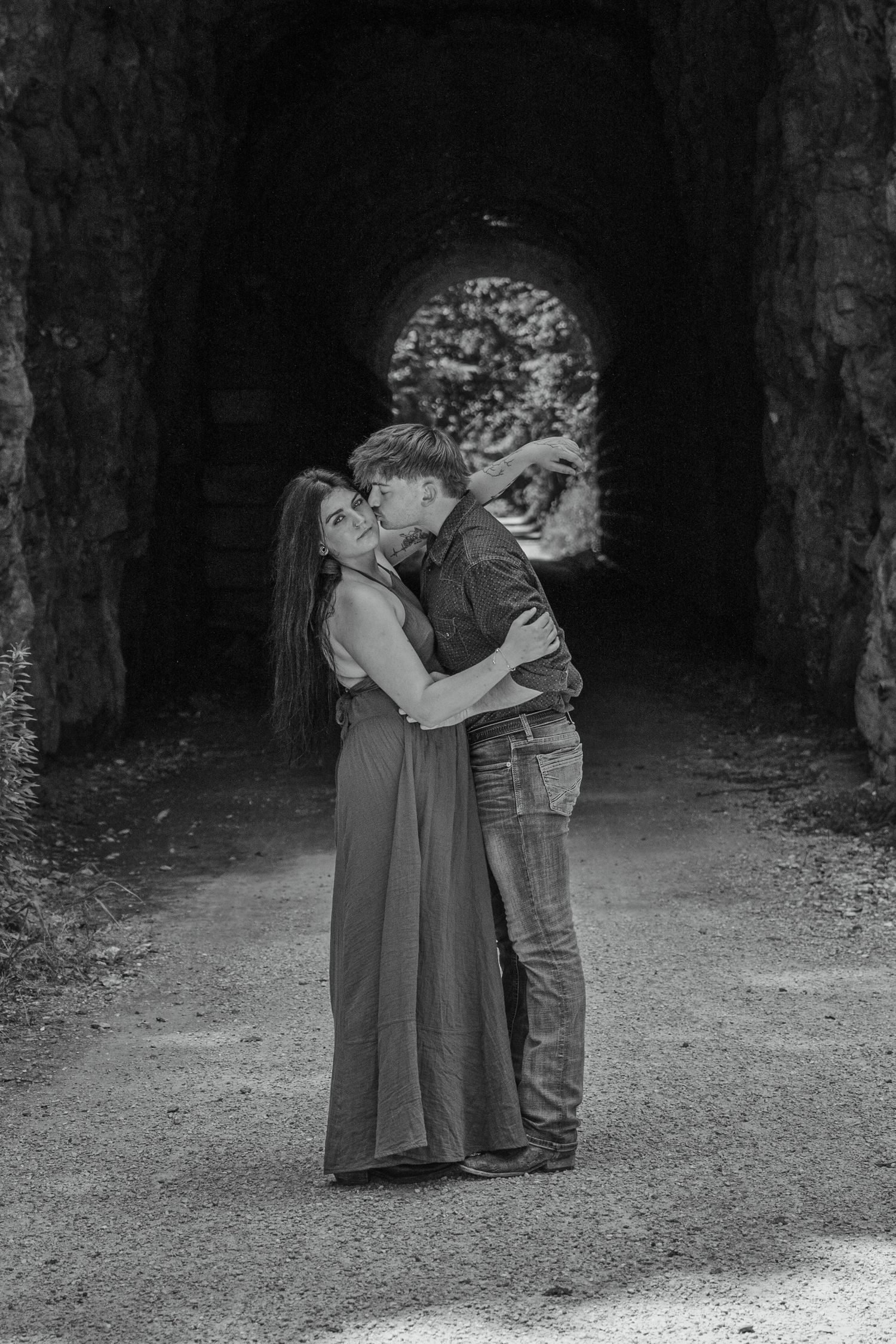 Black and white photo of a romantic couple embracing and kissing inside a stone tunnel archway.