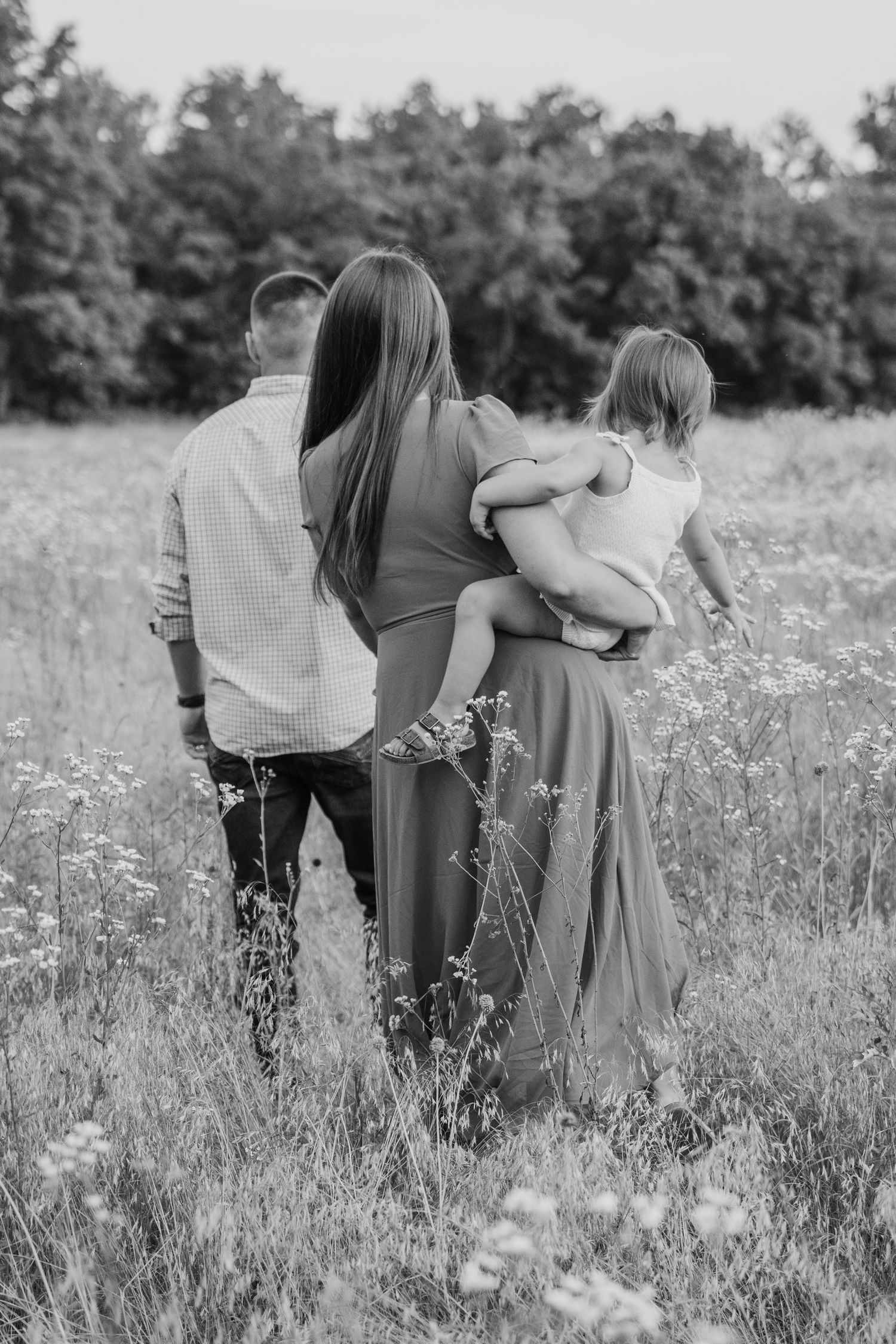Black and white photo of a family walking through a wildflower field, mother carrying child.