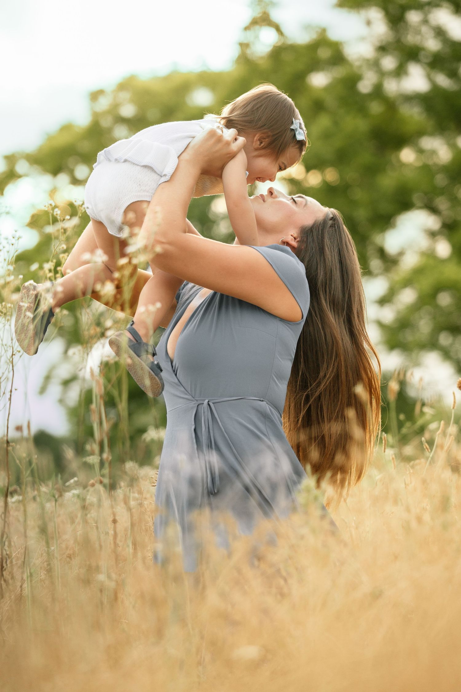 Joyful mother lifting toddler daughter high in the air in a sunny golden field.
