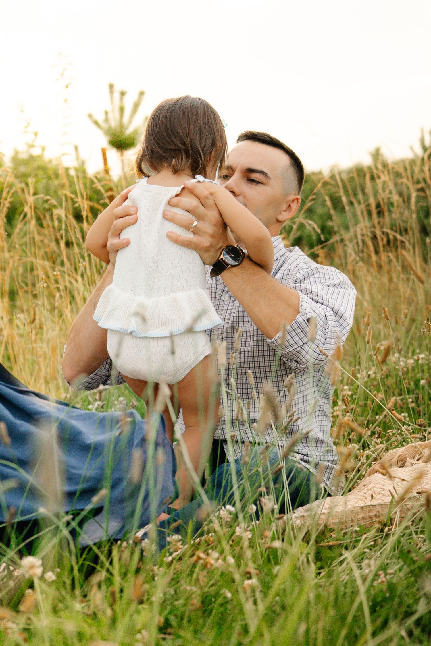 Affectionate father kissing his toddler daughter while sitting together in a golden field.