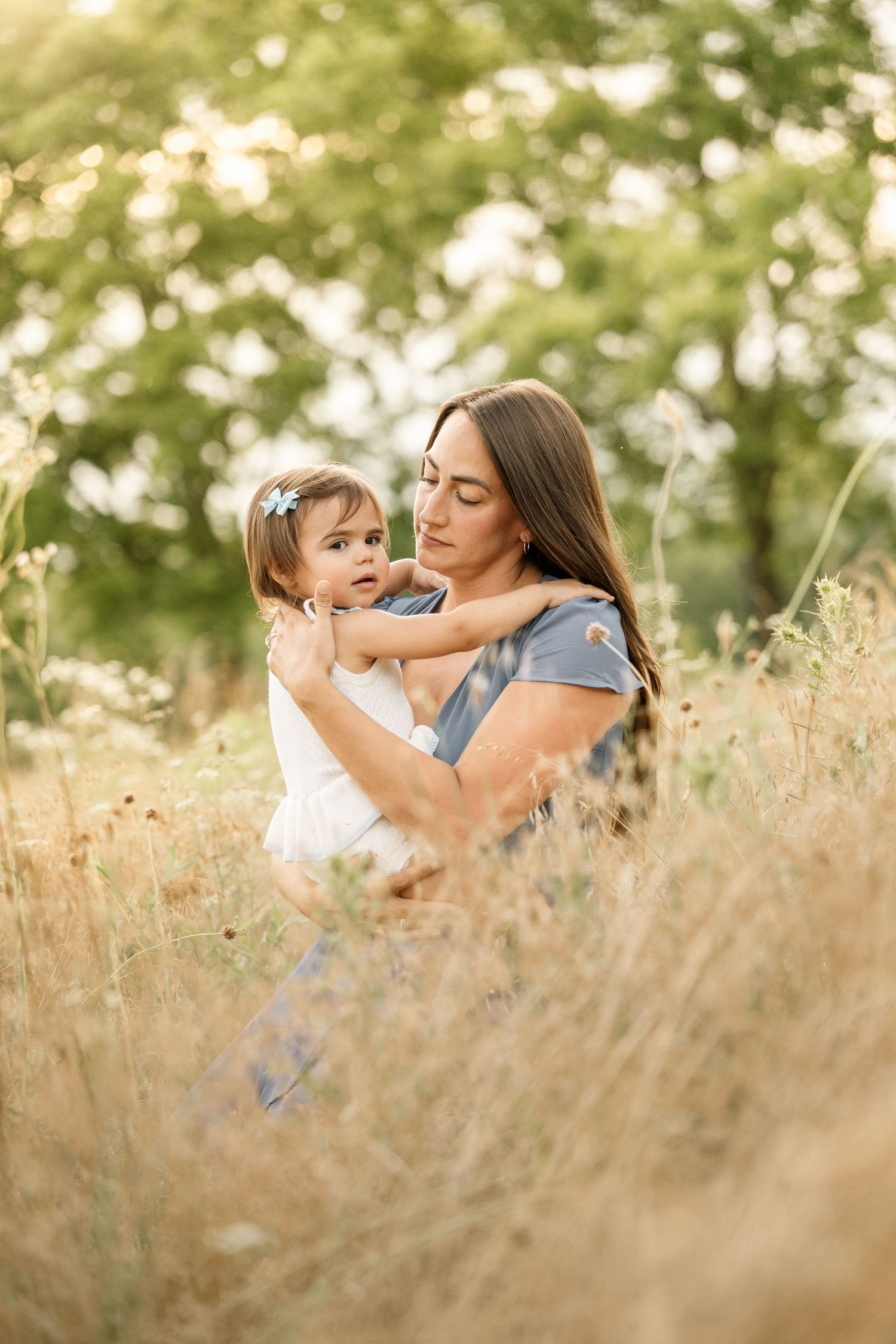 Tender mother holding baby daughter in sun-drenched golden grass field outdoors.