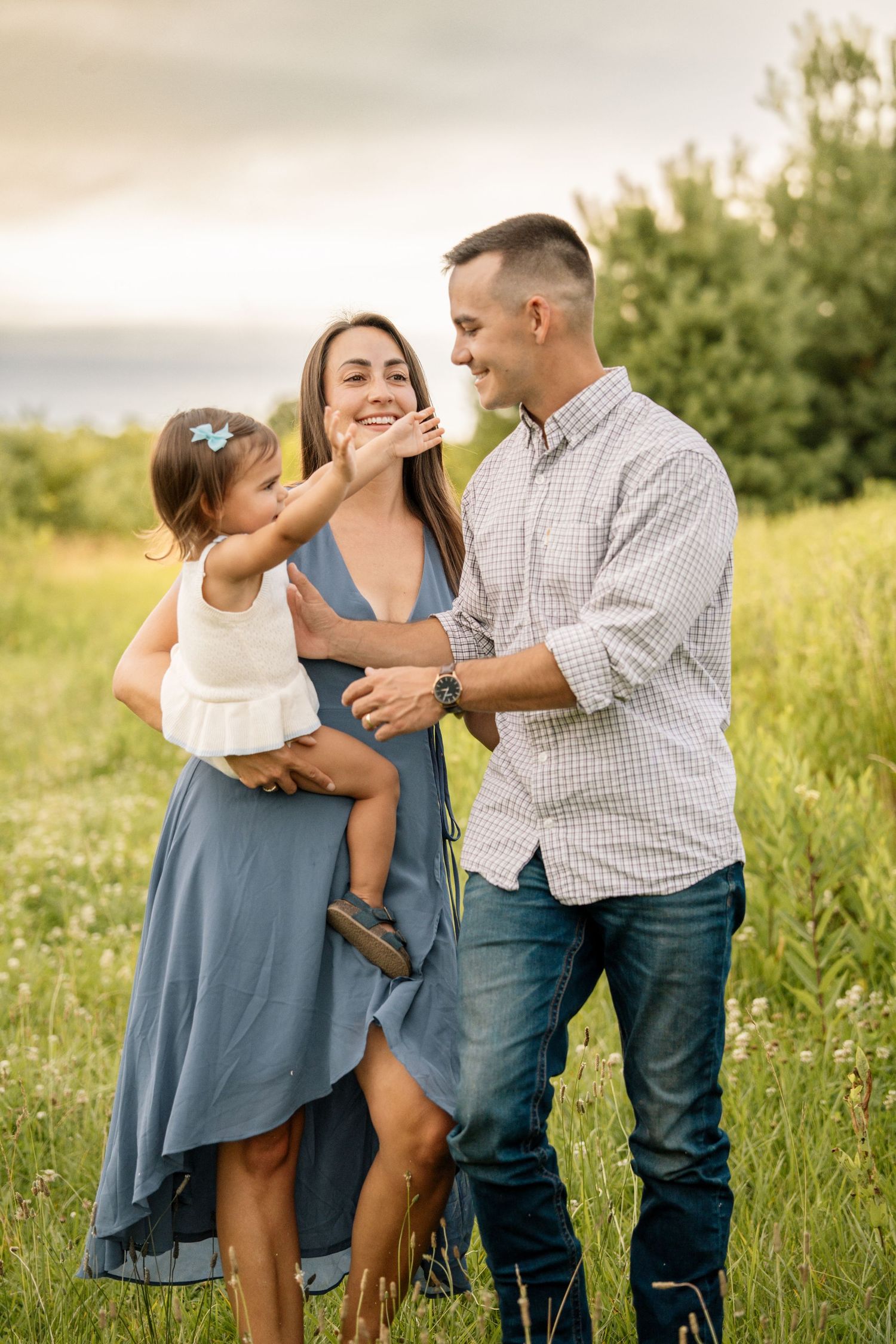 Happy family with father, mother in blue dress, and toddler daughter in sunny meadow.