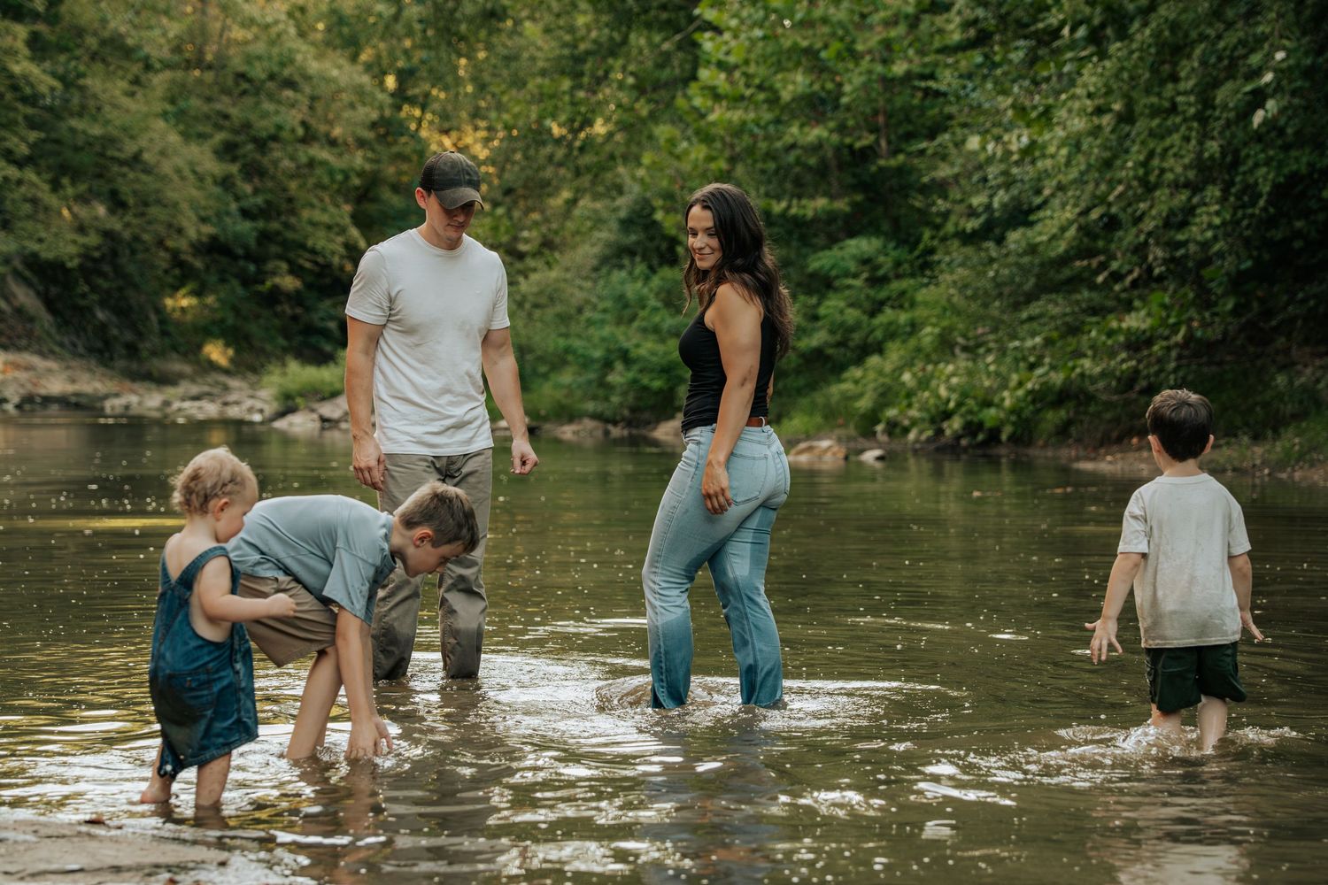 Family of five playing in a shallow creek surrounded by lush green trees.