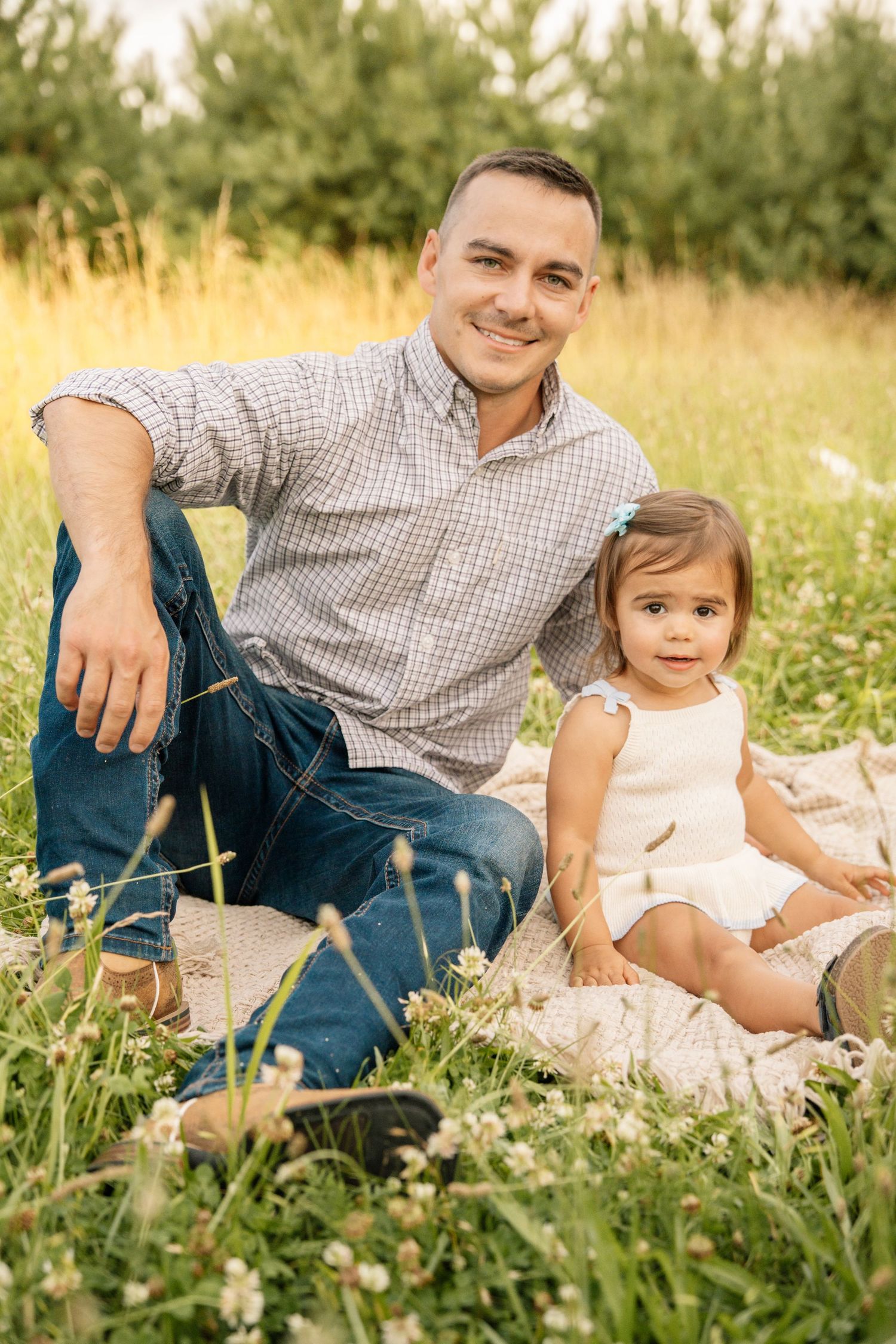 Smiling father sitting on a blanket with his toddler daughter in a sunny meadow.