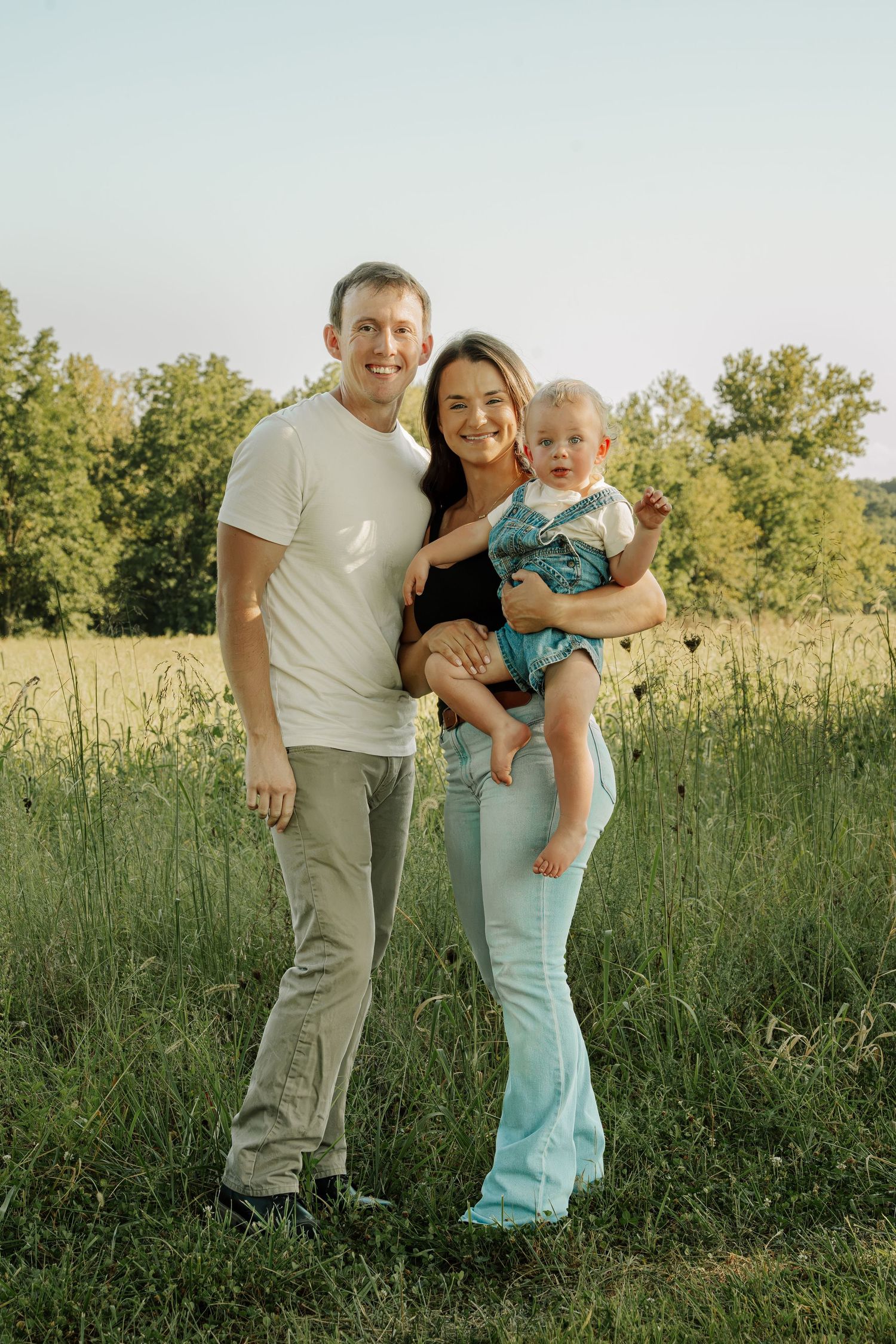 Happy young family with baby posing in a sunny green meadow for an outdoor portrait photo.