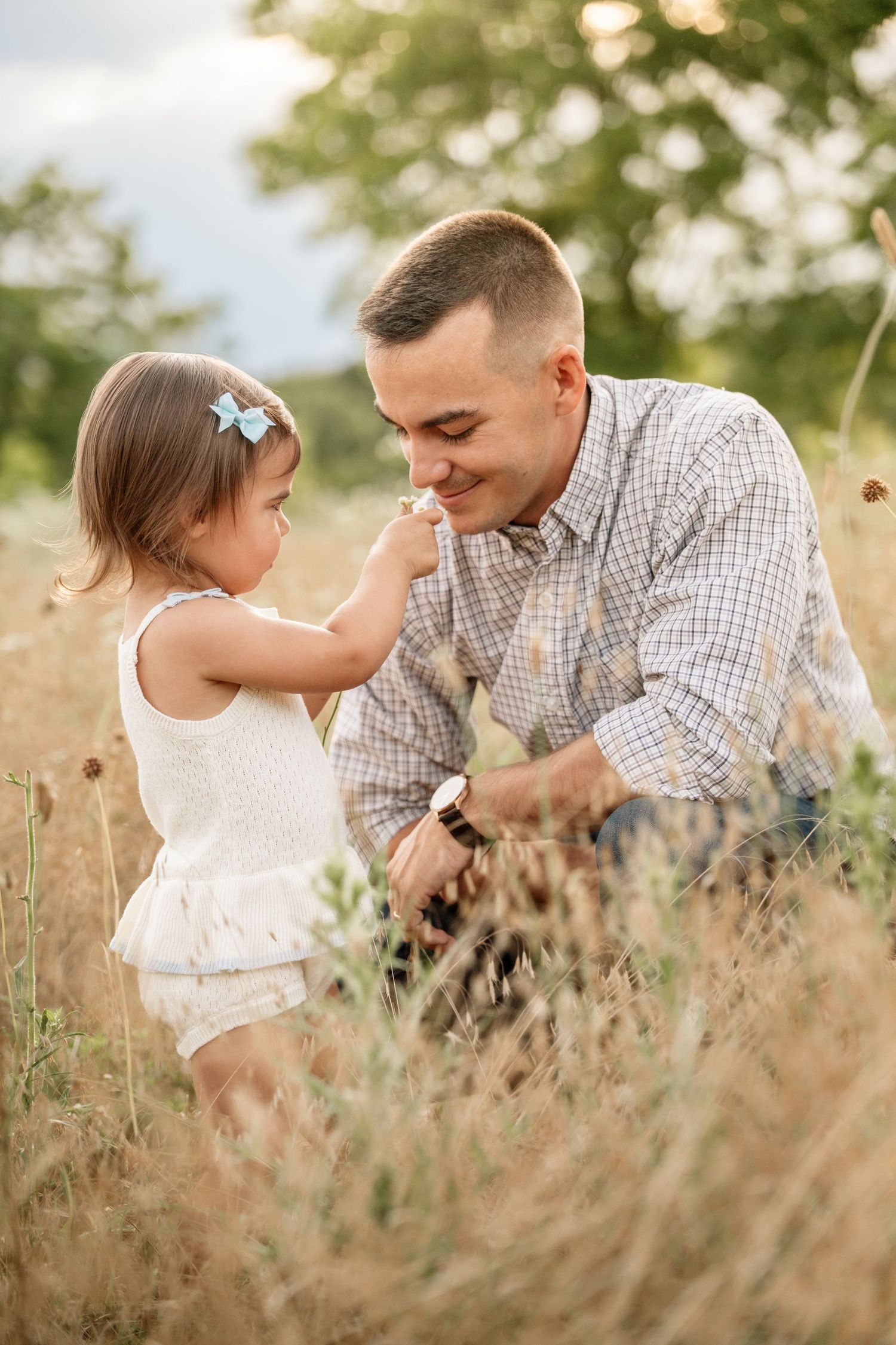 Father smiles as toddler daughter touches his nose in a sunny golden field.