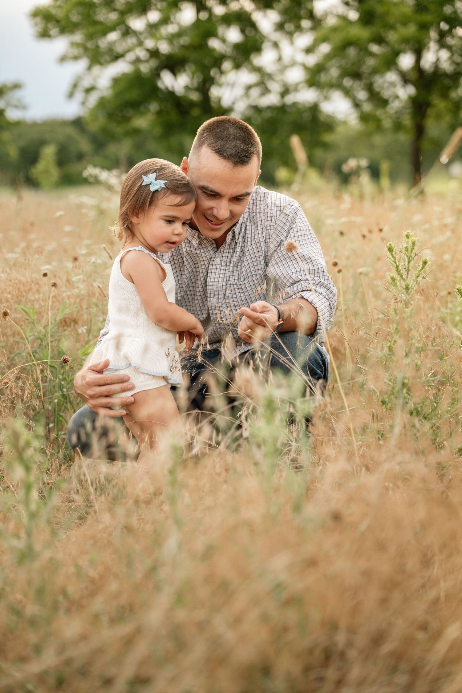 Smiling father crouching with his toddler daughter in a wildflower meadow outdoors.