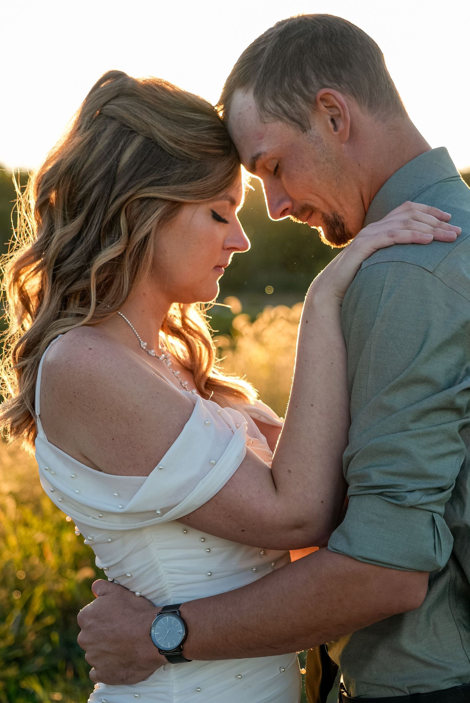 Bride and groom share an intimate forehead touch embrace during a glowing golden hour outdoor wedding shoot.