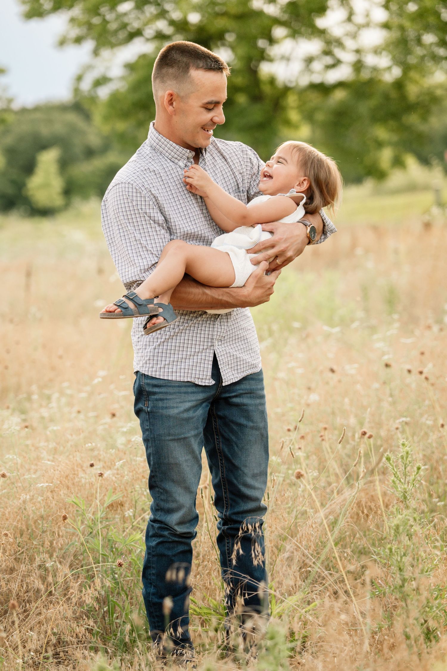 Happy father holding laughing toddler daughter in his arms in a sunny outdoor field.