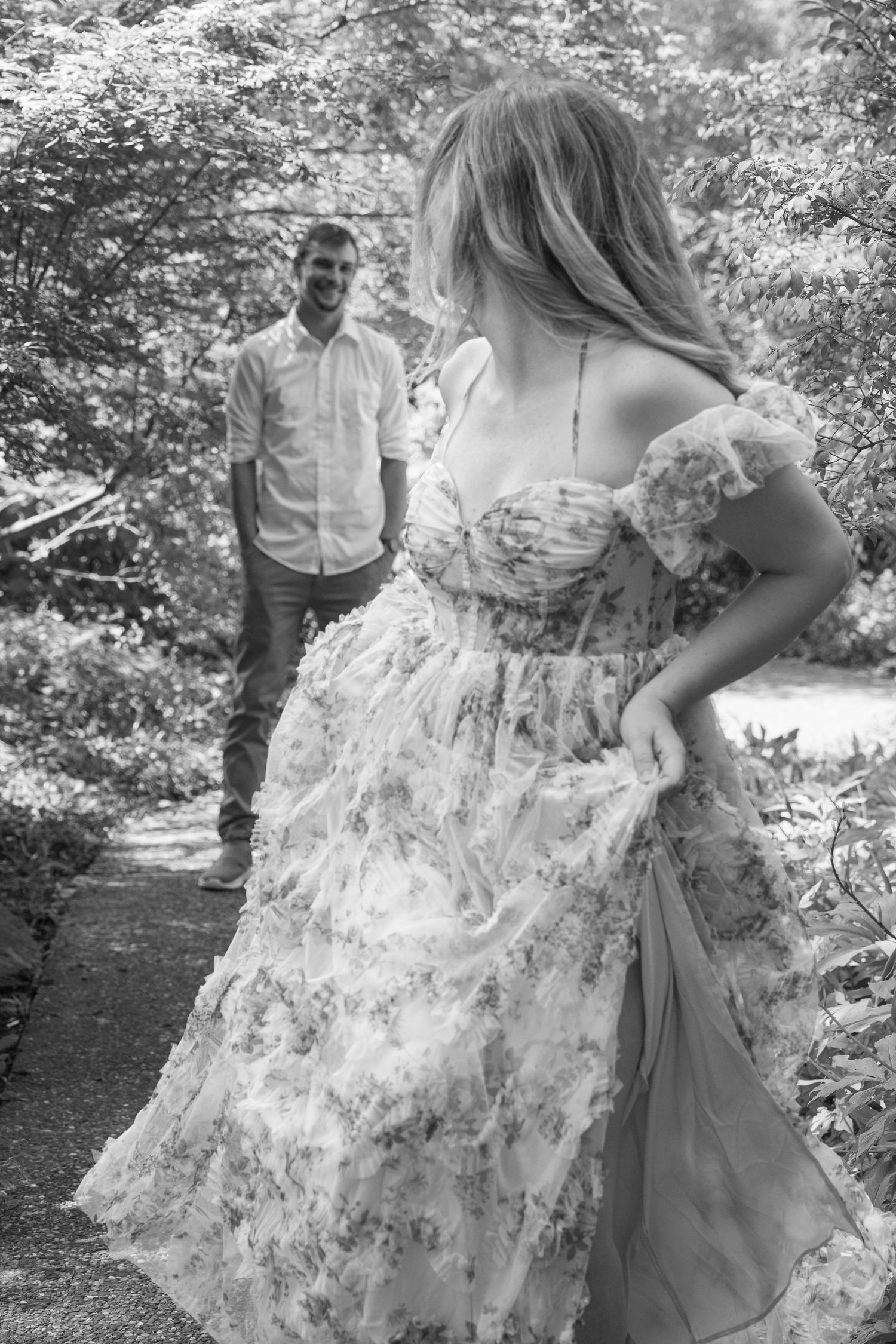 Black and white photo of a woman in a floral dress facing a man on a garden path.