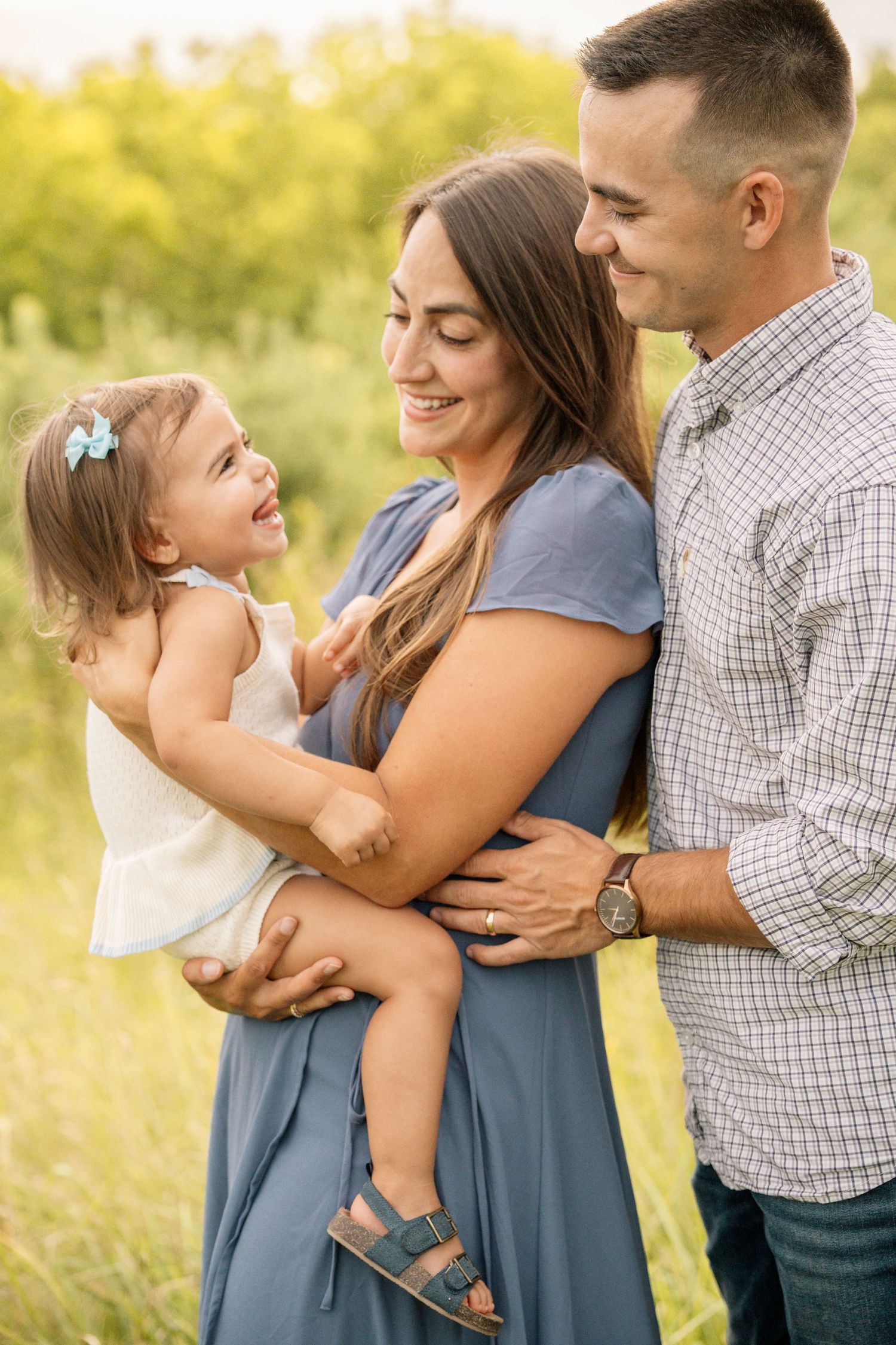 Happy family with toddler daughter sharing a joyful moment together in a lush green outdoor field.