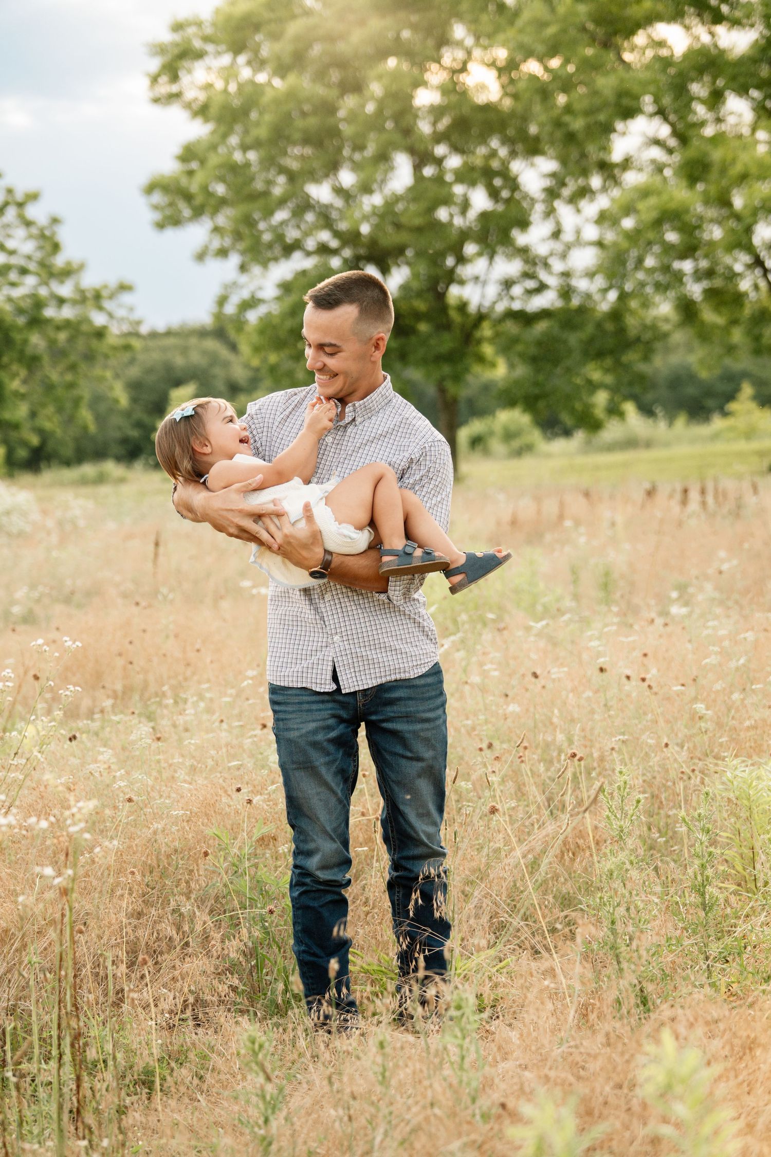 Loving father lifting and smiling at his baby daughter in a sunny wildflower meadow.