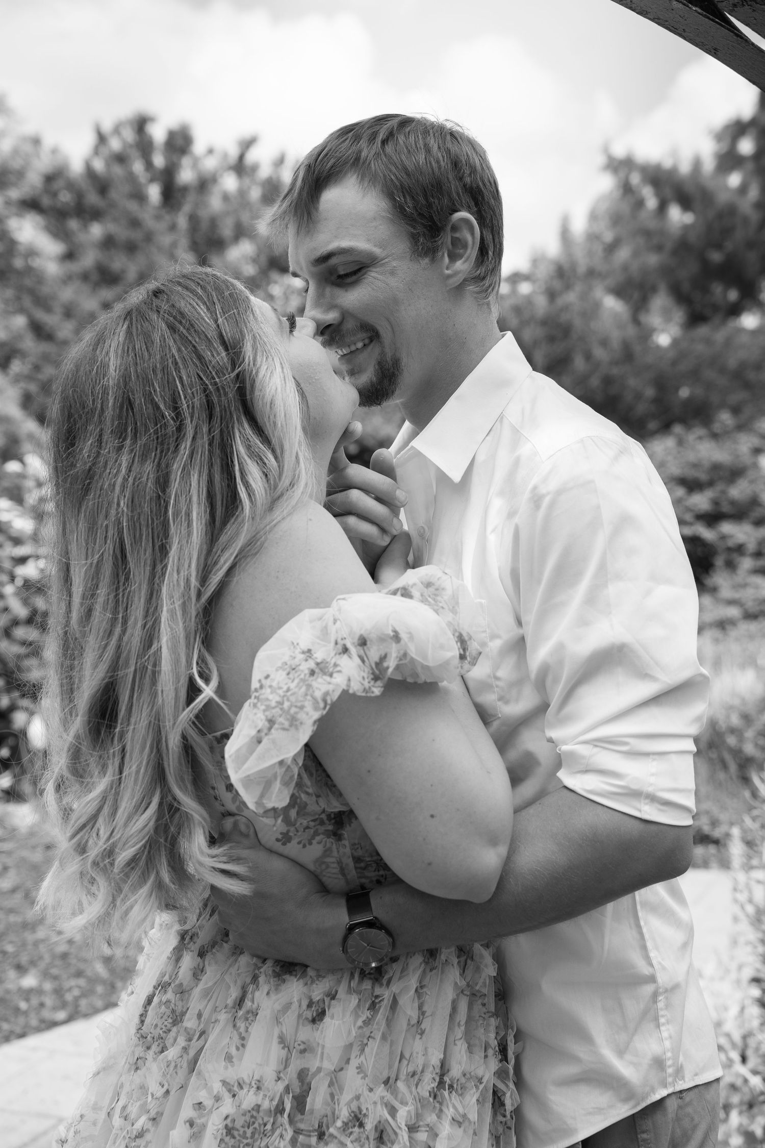 Black and white photo of a laughing couple embracing outdoors in a garden setting.