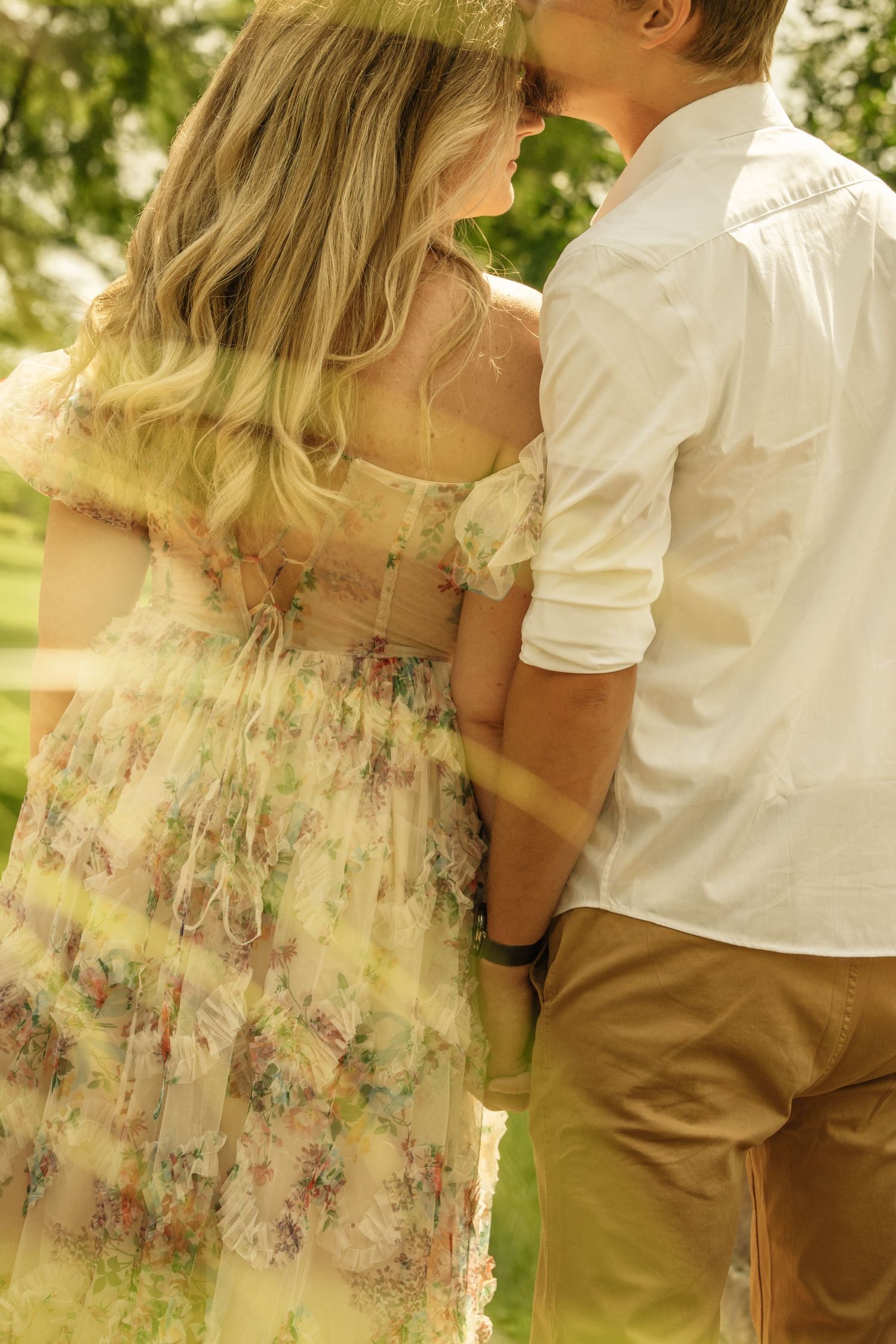 Romantic couple nearly kissing in a lush green garden, woman in floral dress, shot through foliage.