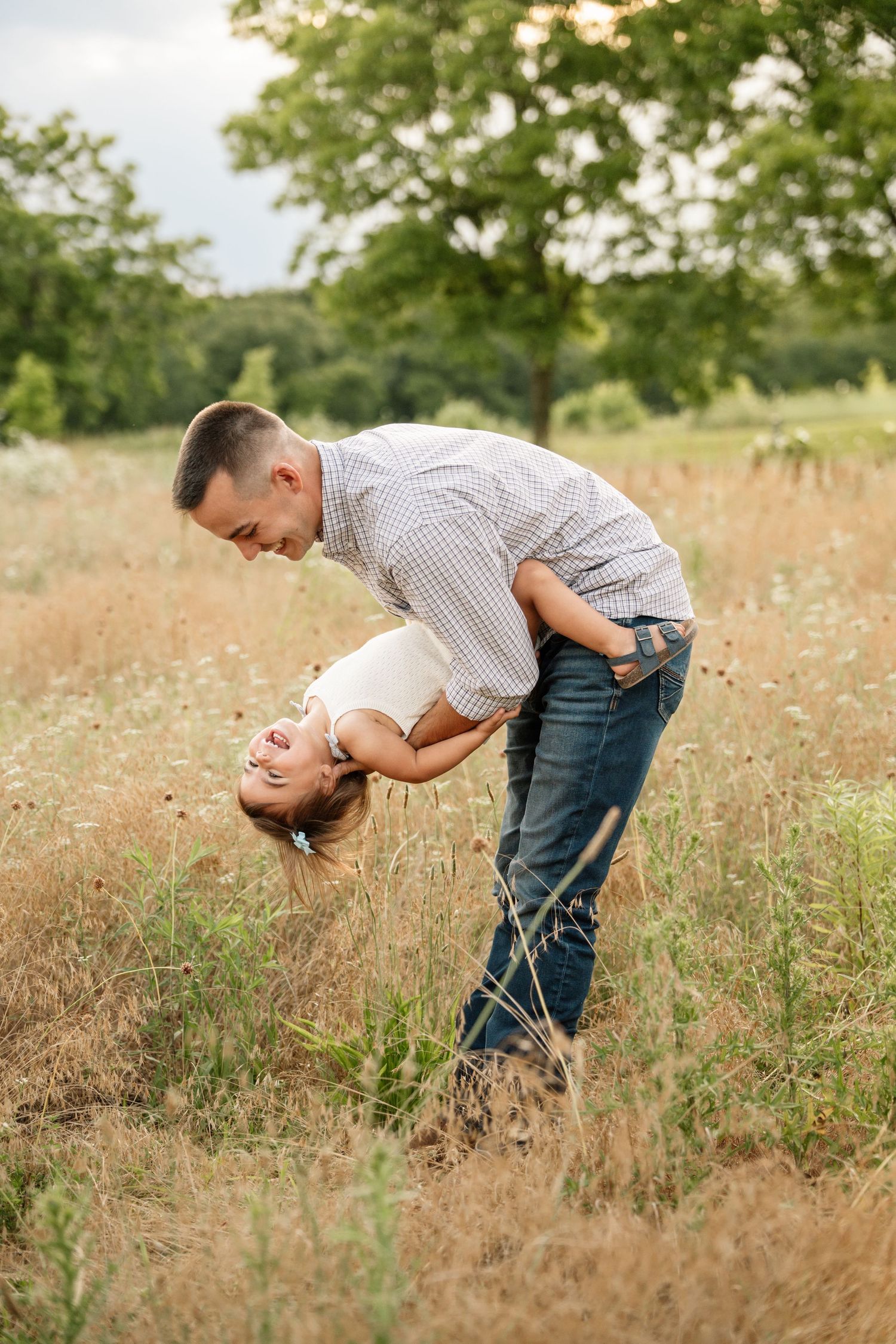 Playful father swinging laughing toddler upside down in golden meadow field.