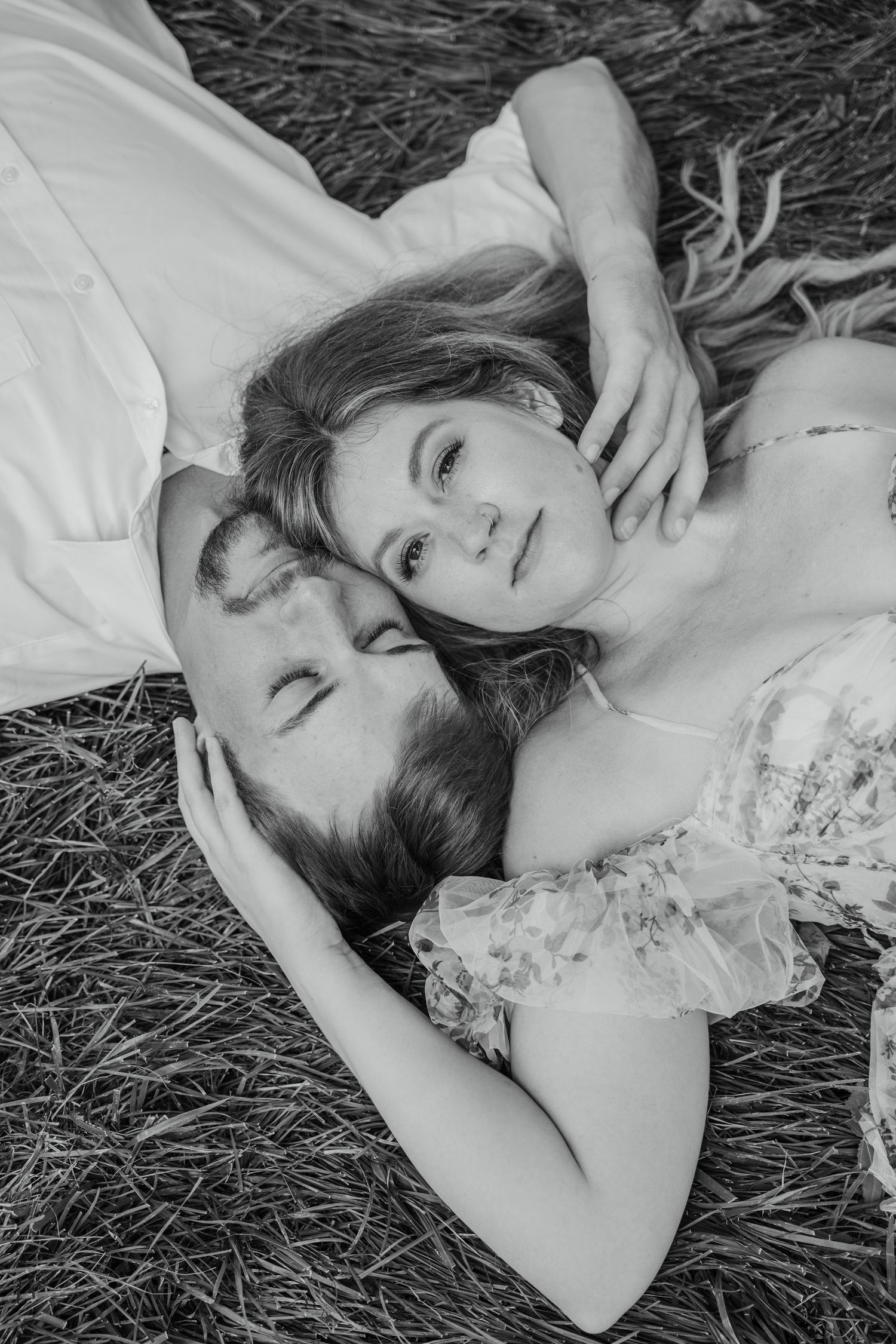 Black and white photo of a couple lying in grass, heads together.