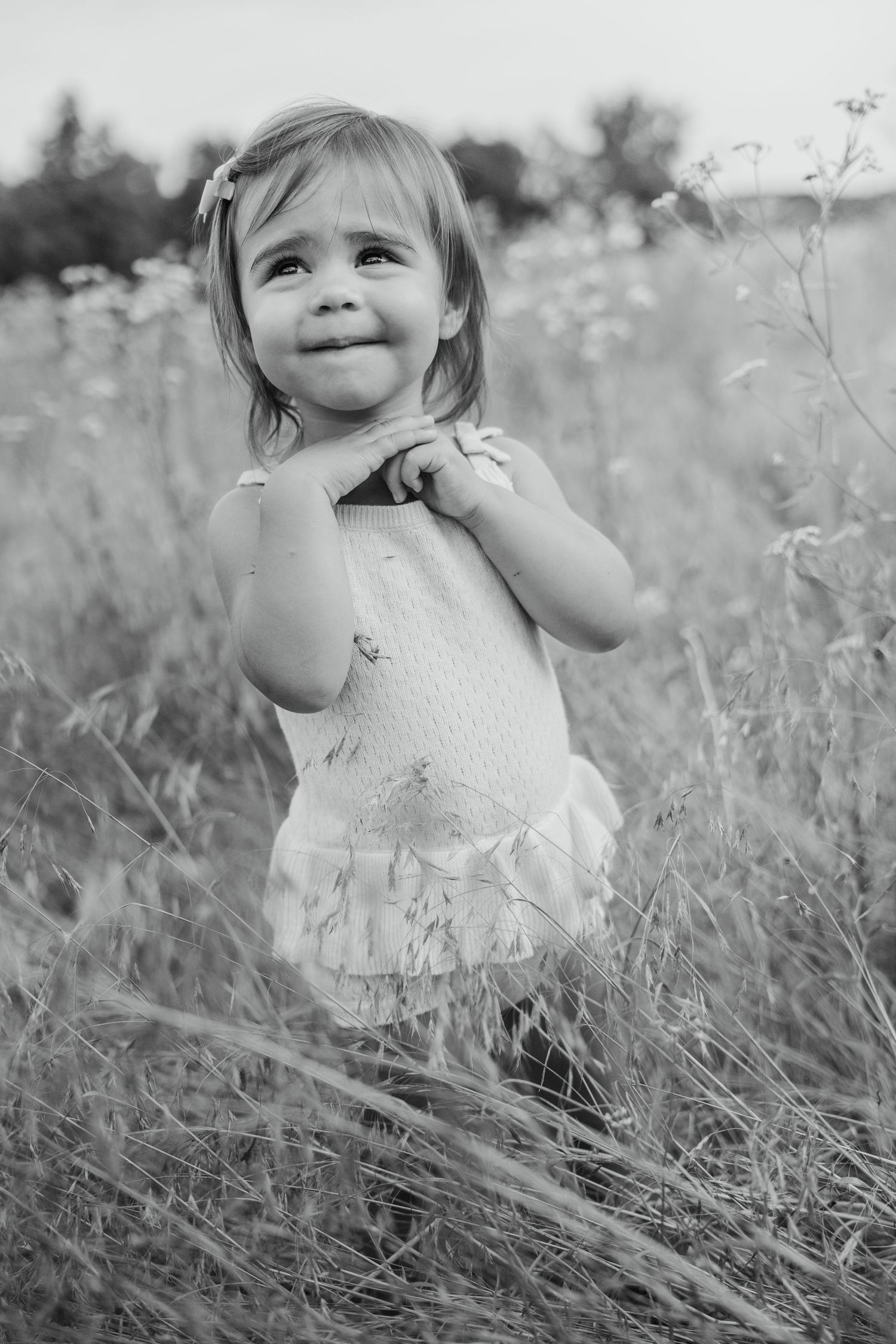 Black and white portrait of a smiling toddler girl holding a flower in a meadow.