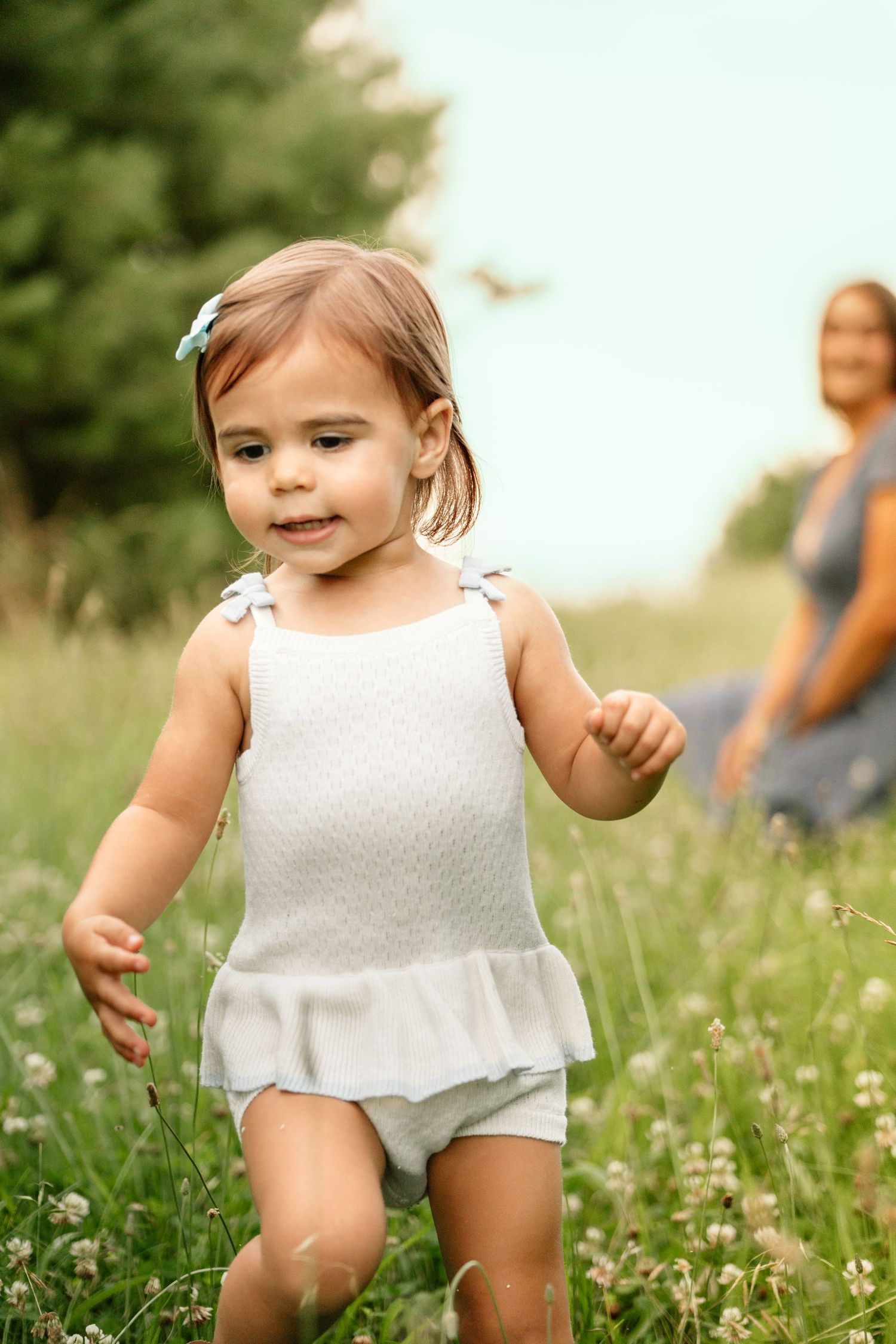 Adorable toddler girl in white romper running through green clover field outdoors.
