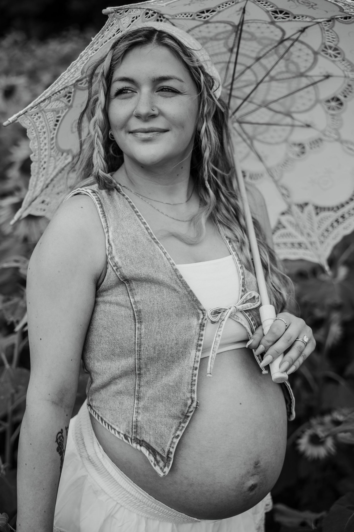 Black and white photo of a smiling pregnant woman holding a lace parasol outdoors.