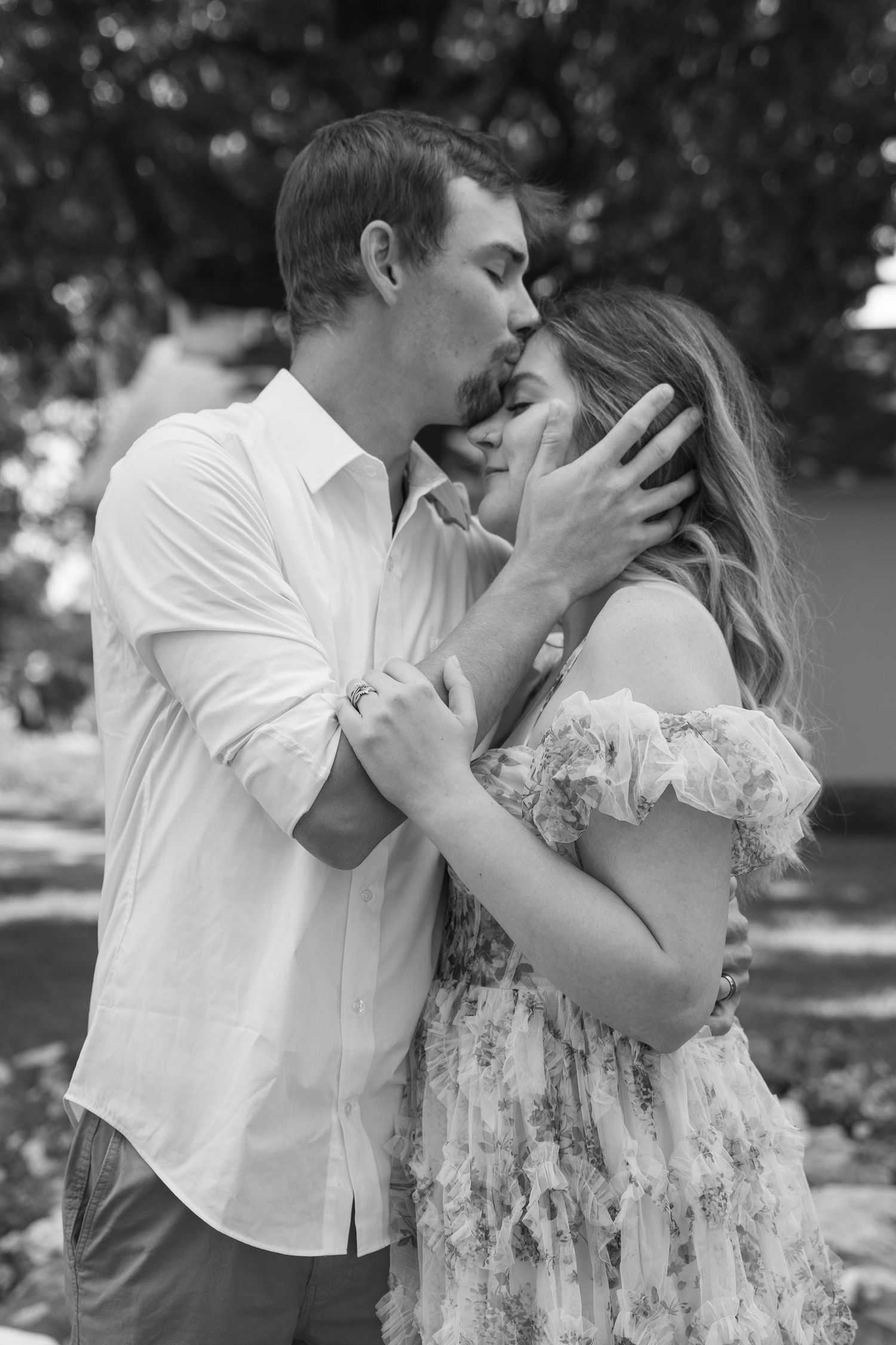 Black and white photo of a couple sharing a tender kiss outdoors, man in white shirt gently holding womans face.