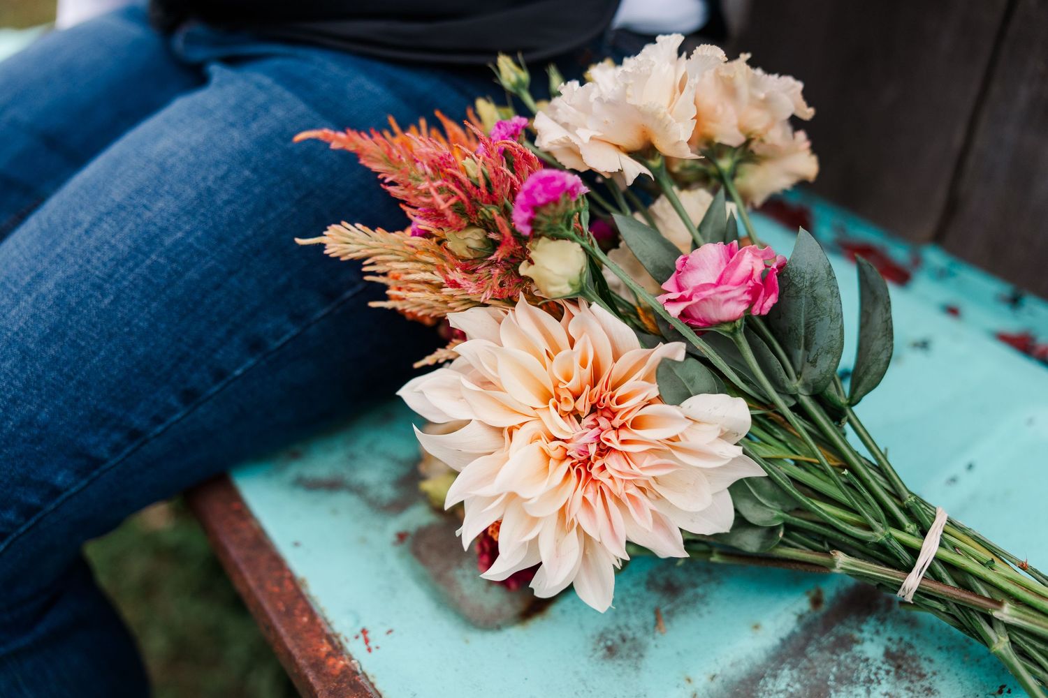 Bouquet of peach dahlias and colorful mixed flowers resting on a rustic turquoise bench.