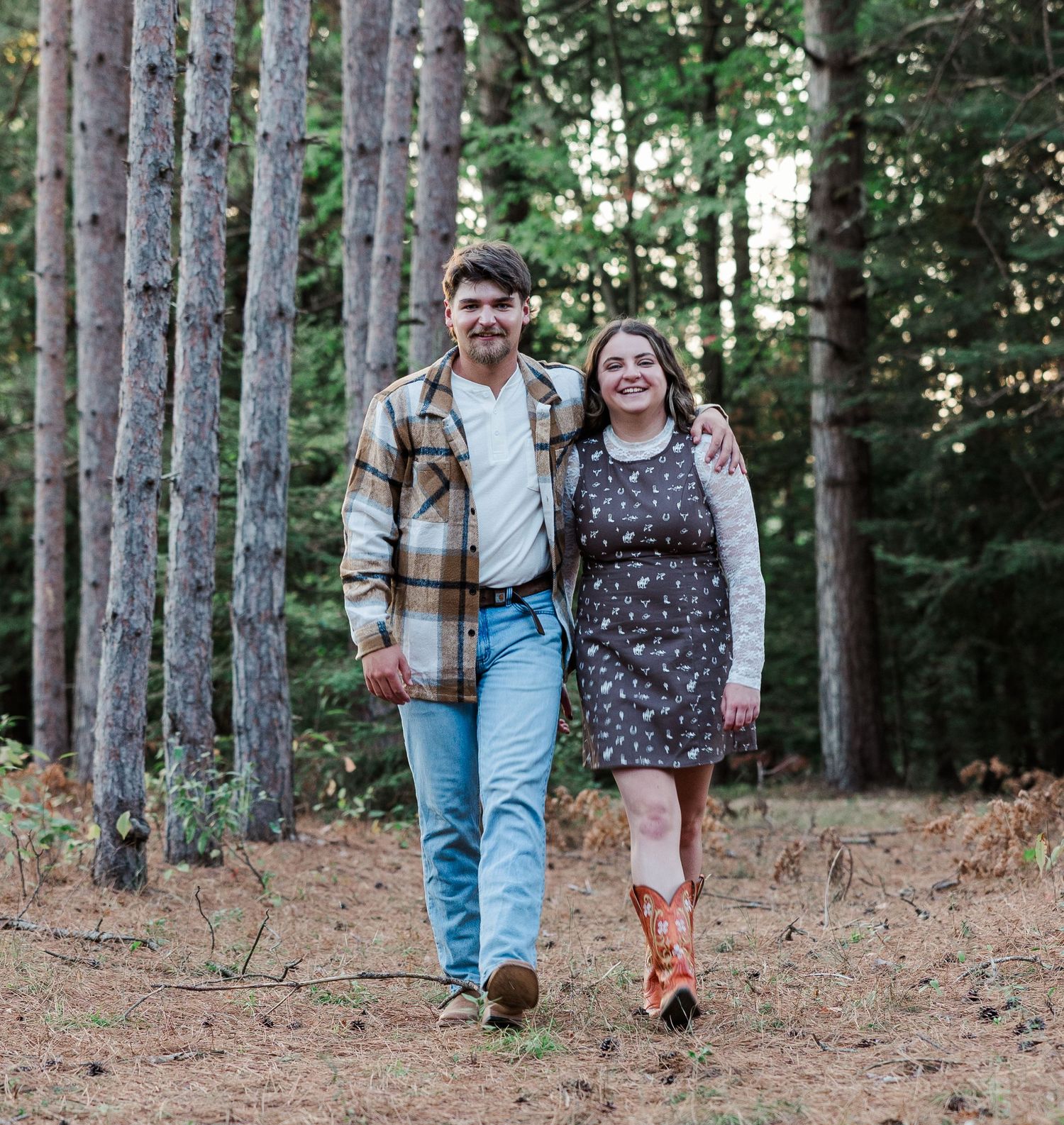 Young couple walking hand in hand through a sunlit pine forest on a dirt path.