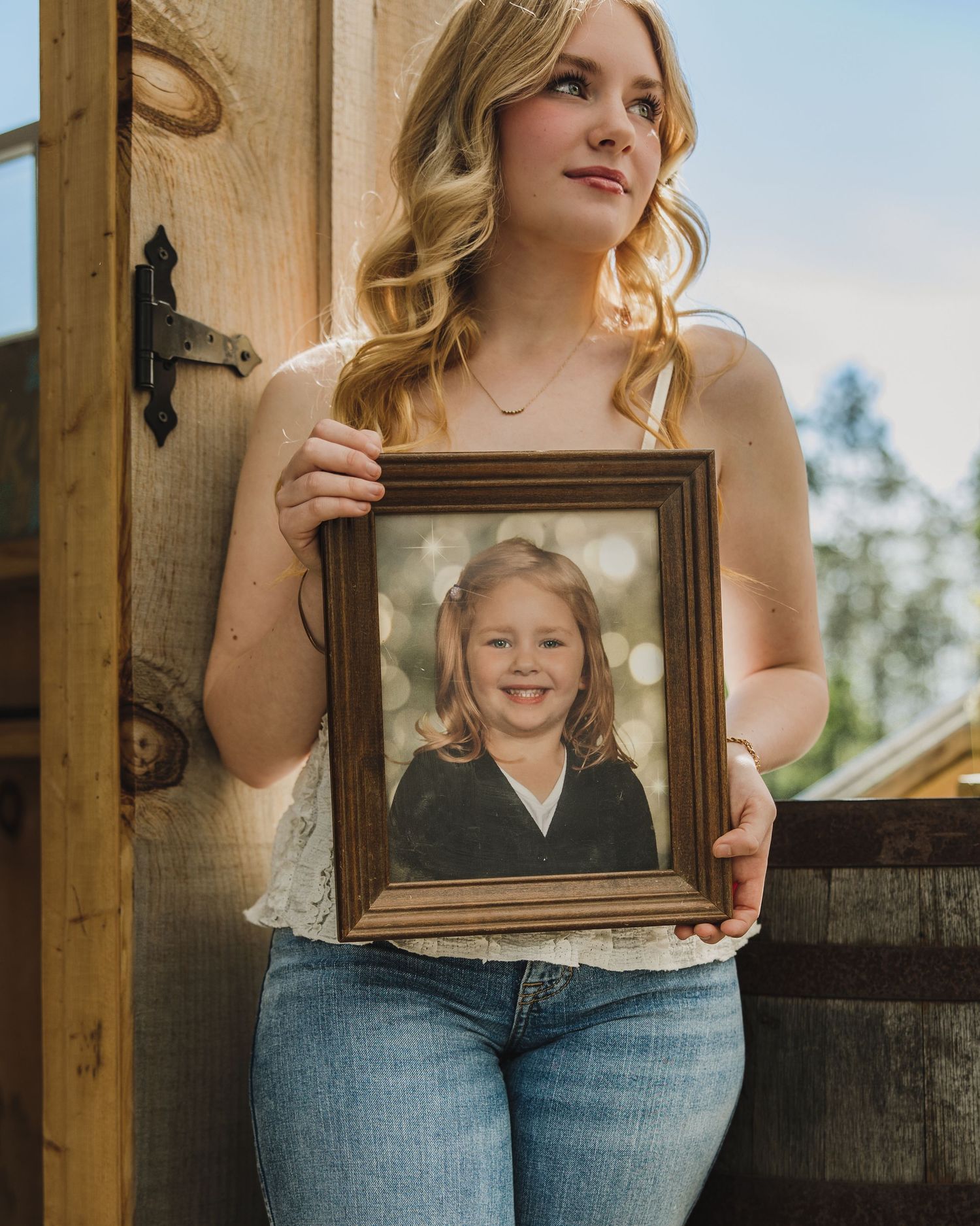 Young blonde woman holding a framed childhood photo of herself during a senior portrait session.