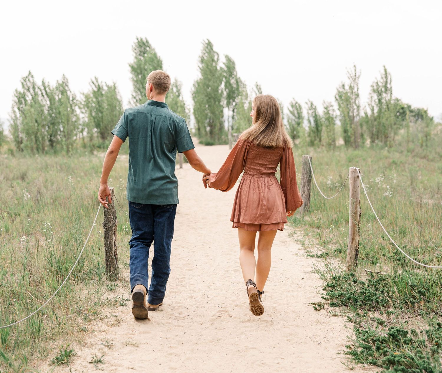 A couple walks hand-in-hand down a sandy path surrounded by lush greenery.