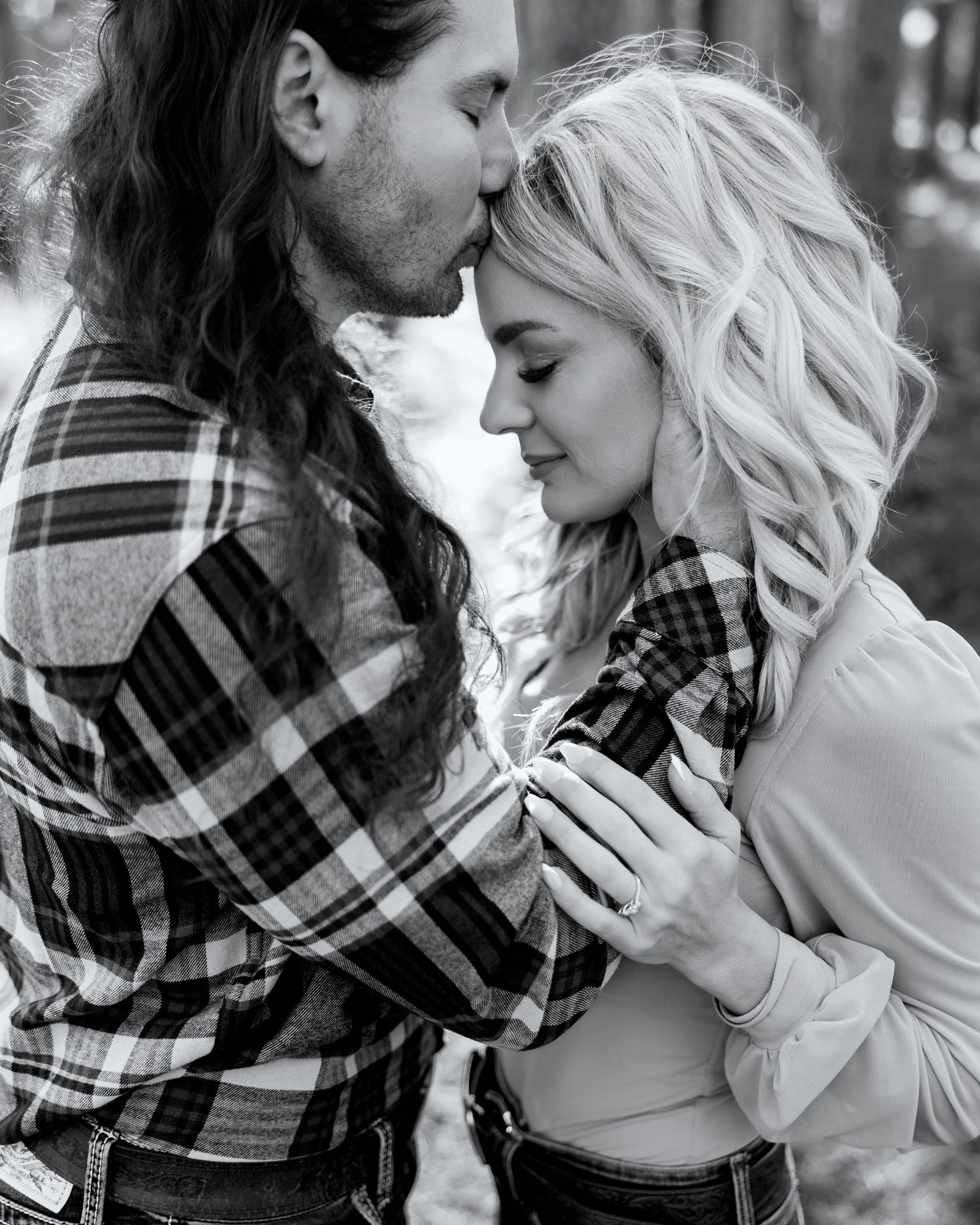 Black and white photo of a romantic couple in plaid shirts sharing an intimate moment outdoors.