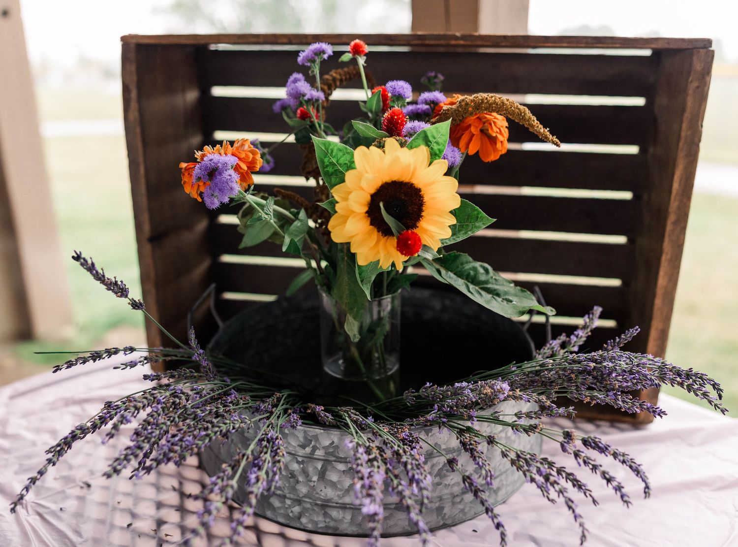 Rustic sunflower and lavender floral centerpiece arrangement in wooden crate on lace tablecloth.