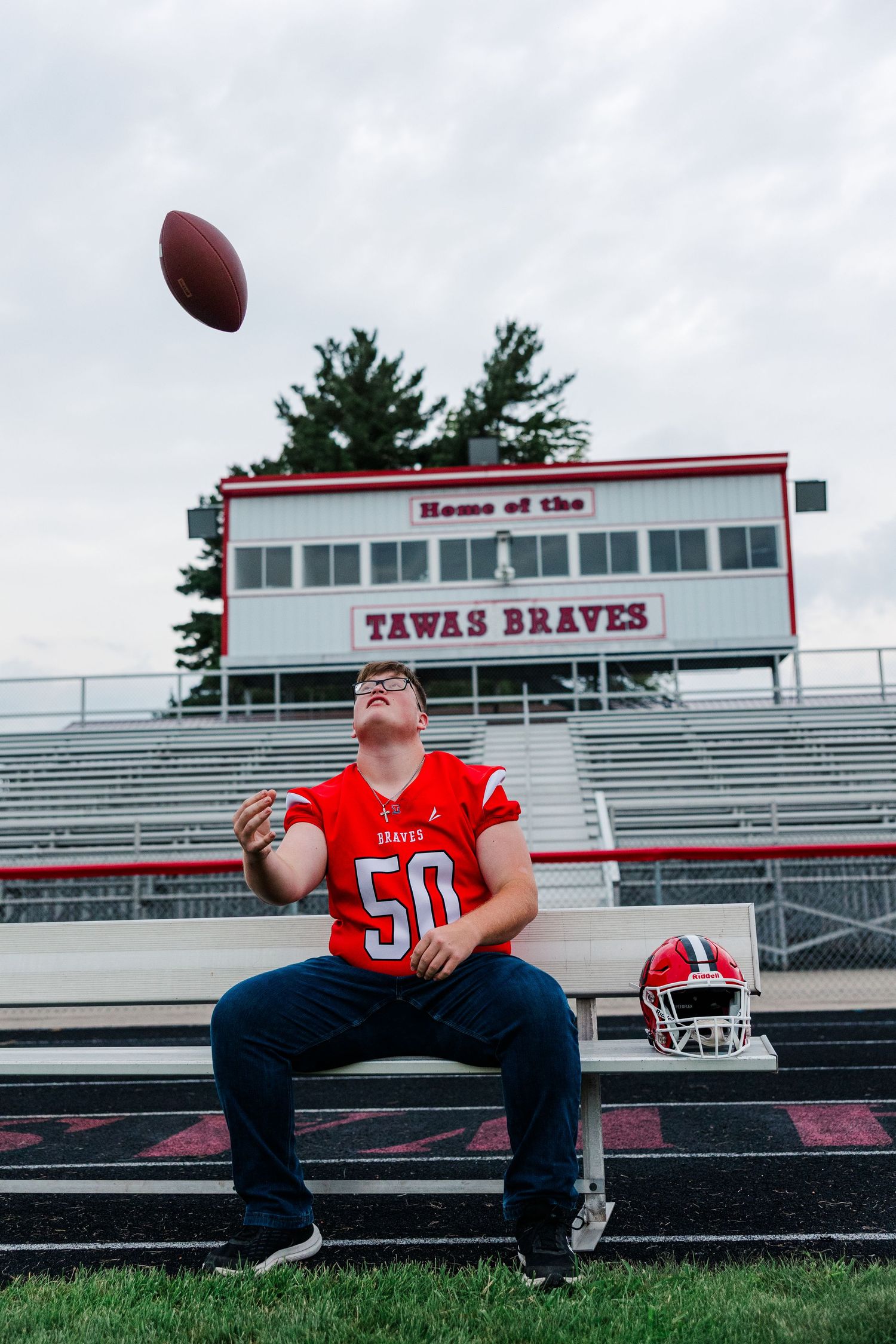 Tawas Braves football player #50 tossing a ball in bleachers at Tawas Area High School stadium.