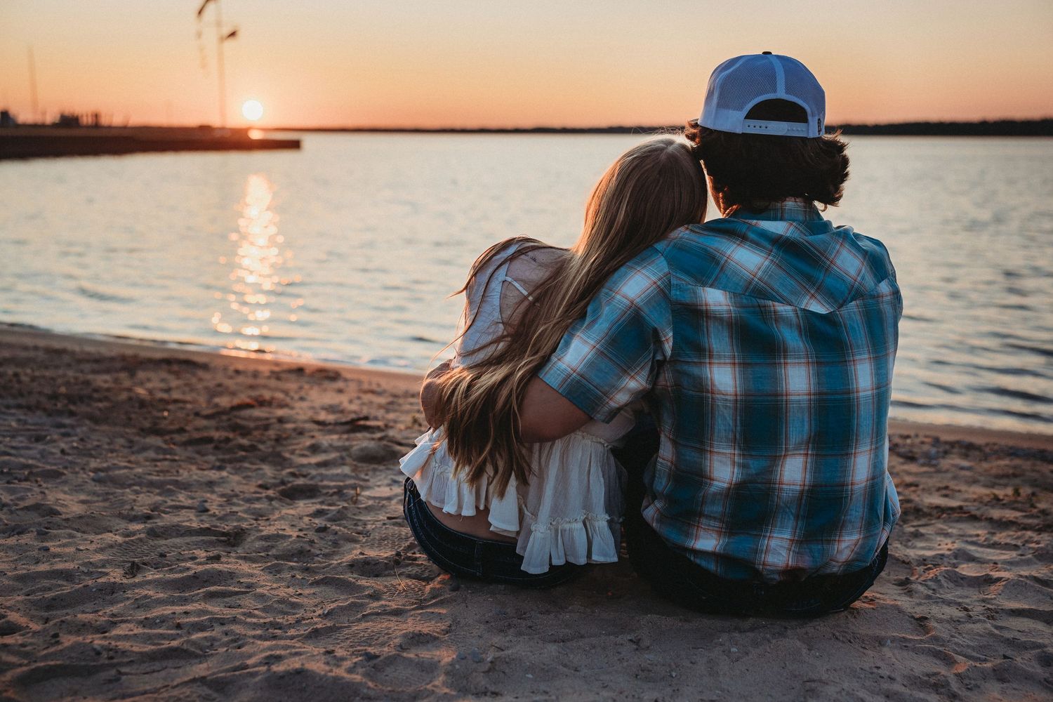 Couple sitting together on a sandy beach watching a beautiful sunset over calm water.