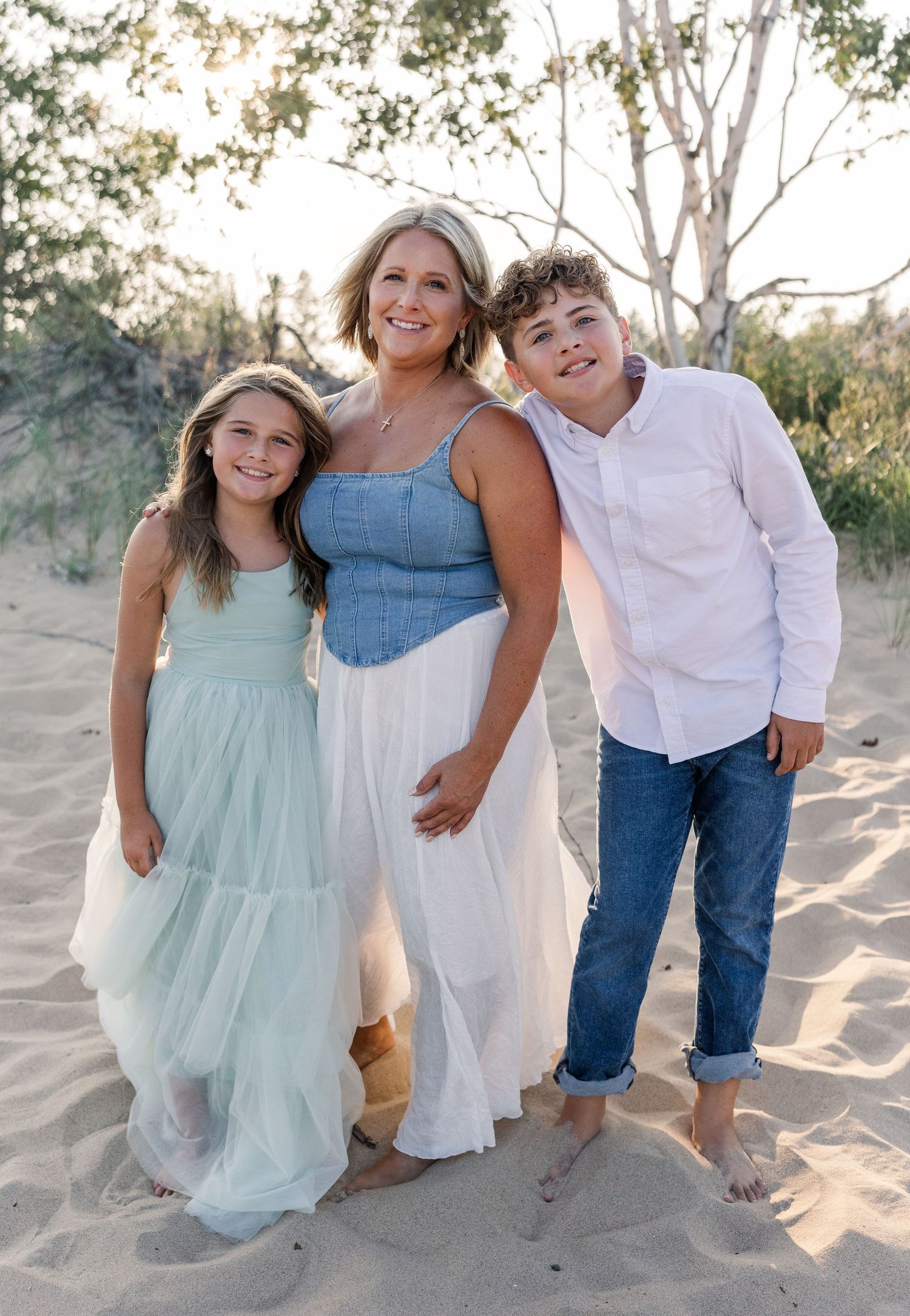 A smiling mother poses with her two children on a sandy beach at sunset.