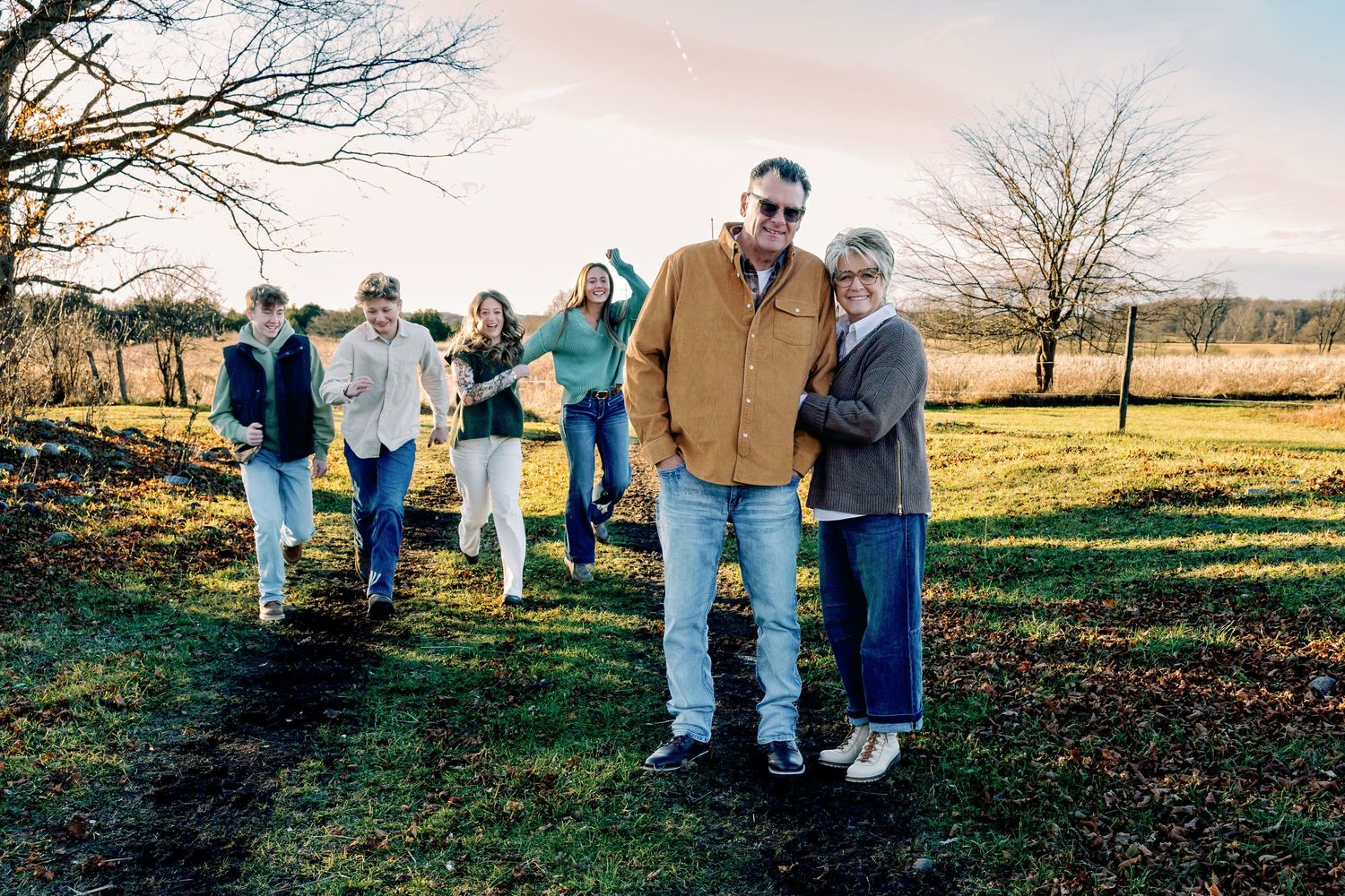 A multigenerational family walks together on a grassy path during golden hour.
