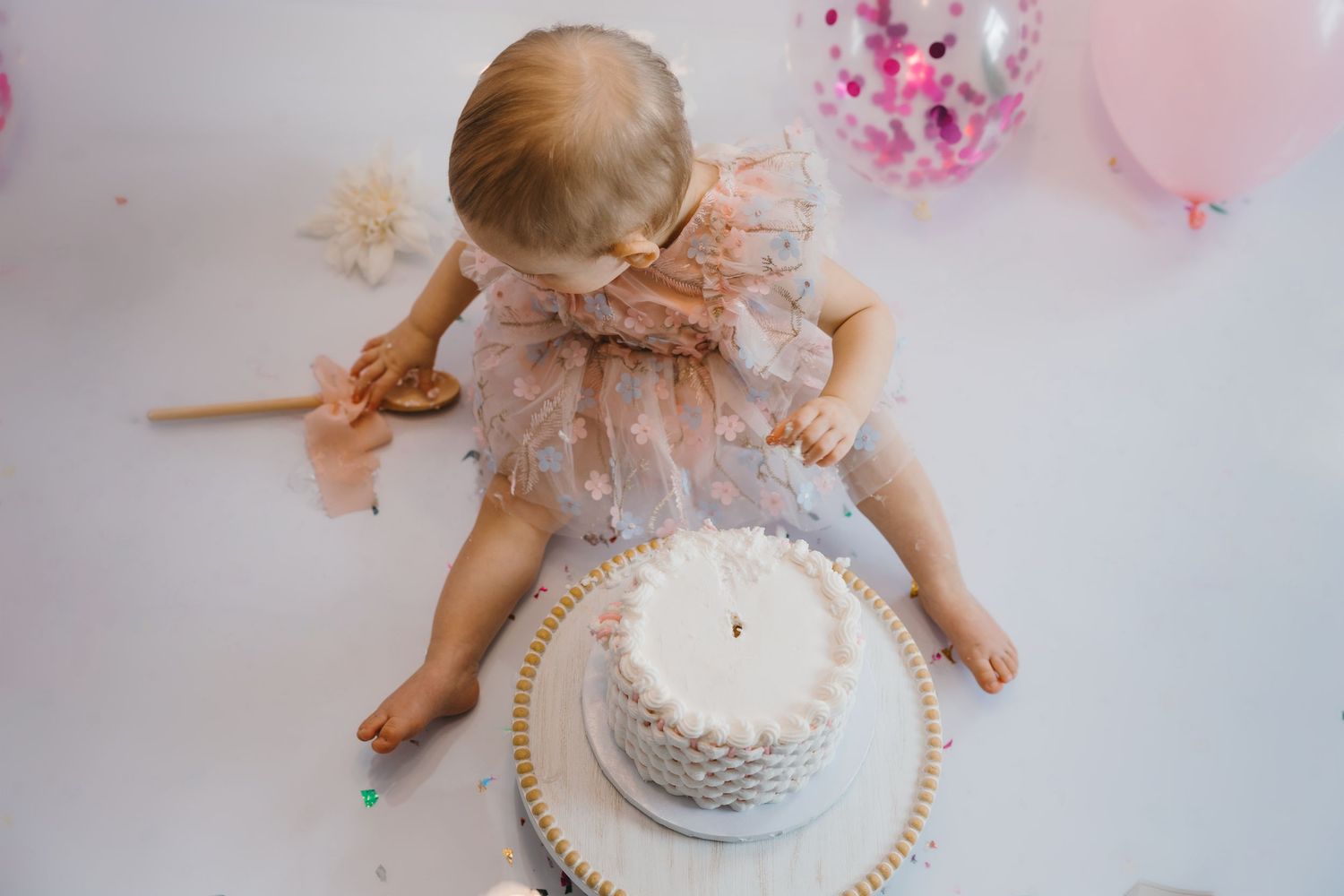 Overhead view of baby girl in pink tutu dress touching white cake at first birthday cake smash session.