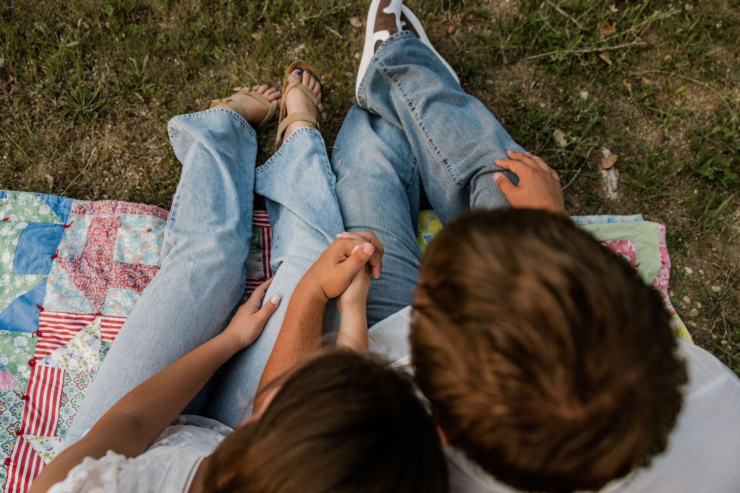 Couple relaxing on a colorful quilt blanket outdoors, holding hands while lying on green grass.
