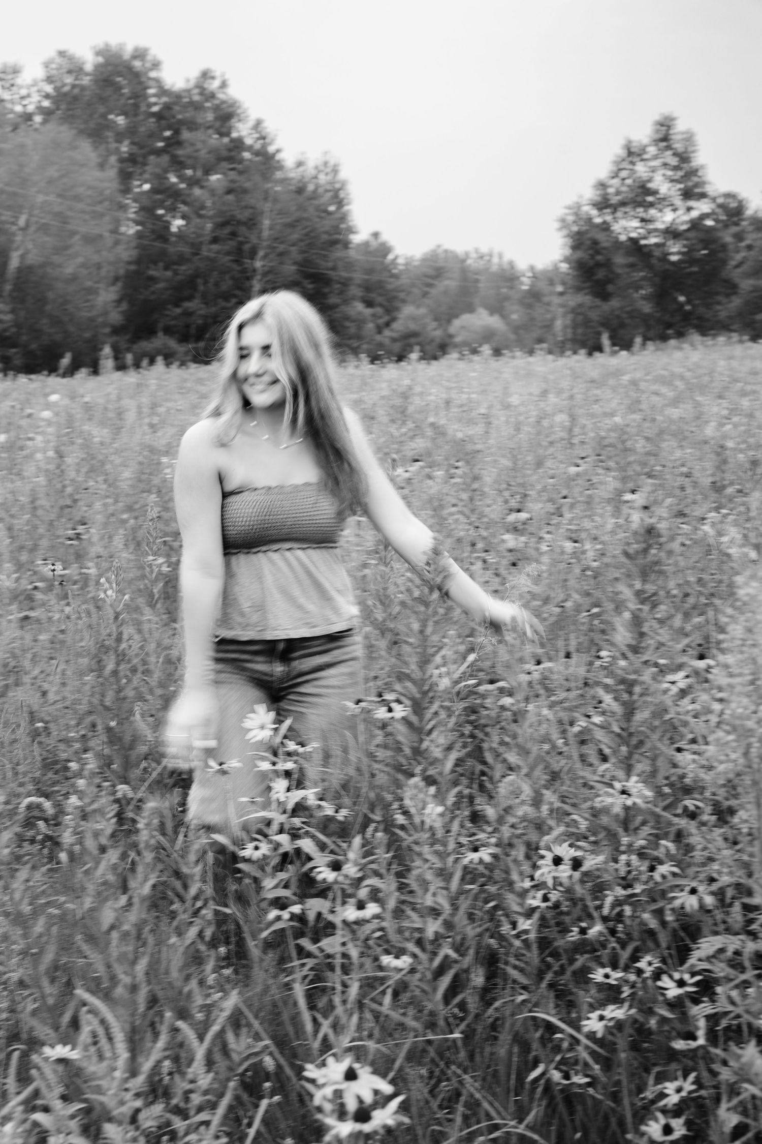 Young woman smiling in a wildflower meadow, black and white photo with trees in background.