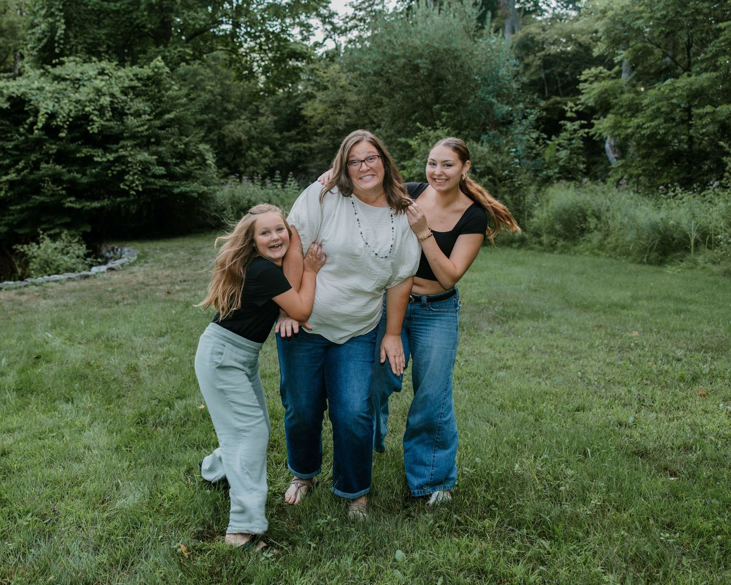 Woman and two girls smiling together in a lush green outdoor setting.