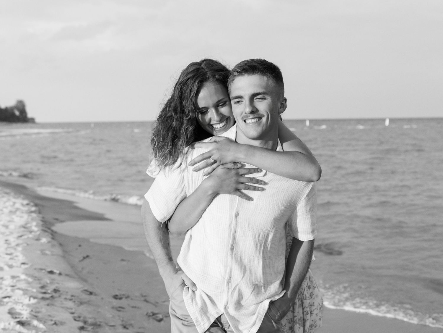 Happy couple embracing on a sandy beach in black and white photo, smiling joyfully by the ocean.