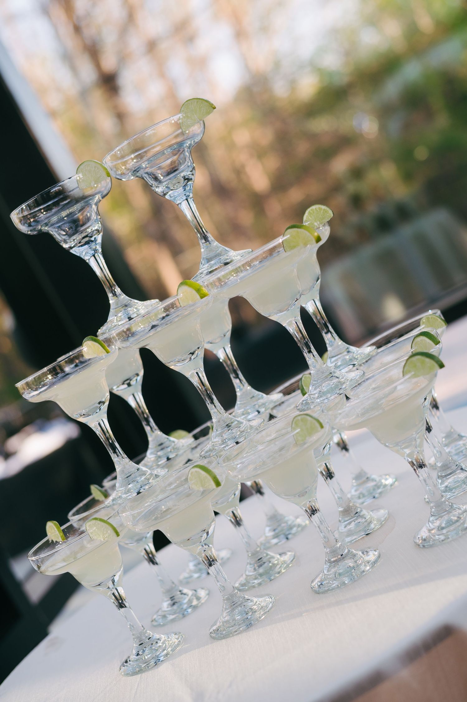 Elegant margarita tower display with lime garnishes on white tablecloth at outdoor event.
