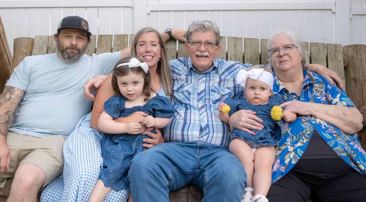 Multi-generational family portrait with grandparents, parents, and two young girls sitting together on porch steps.