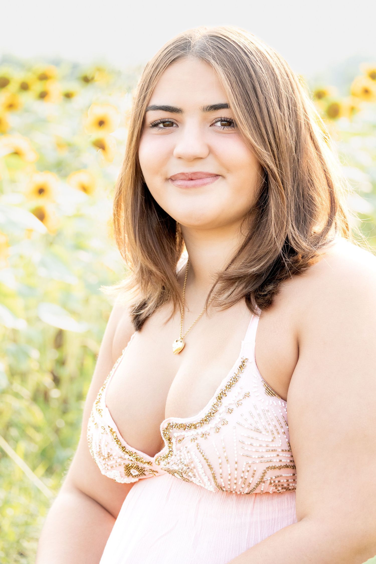 Young woman in pink sequin top smiling in a sunflower field, portrait photography.